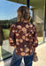 Bring a fresh twist to your fall wardrobe with this beautifully detailed blouse from Fate. Featuring a rich brown leopard-inspired print accented with a soft neutral floral design, this feminine top effortlessly blends bold style with timeless charm. The button-front silhouette is finished with a subtle ruffle neckline and delicate ruffle details throughout the front and back for added texture. 