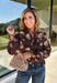 Bring a fresh twist to your fall wardrobe with this beautifully detailed blouse from Fate. Featuring a rich brown leopard-inspired print accented with a soft neutral floral design, this feminine top effortlessly blends bold style with timeless charm. The button-front silhouette is finished with a subtle ruffle neckline and delicate ruffle details throughout the front and back for added texture. 