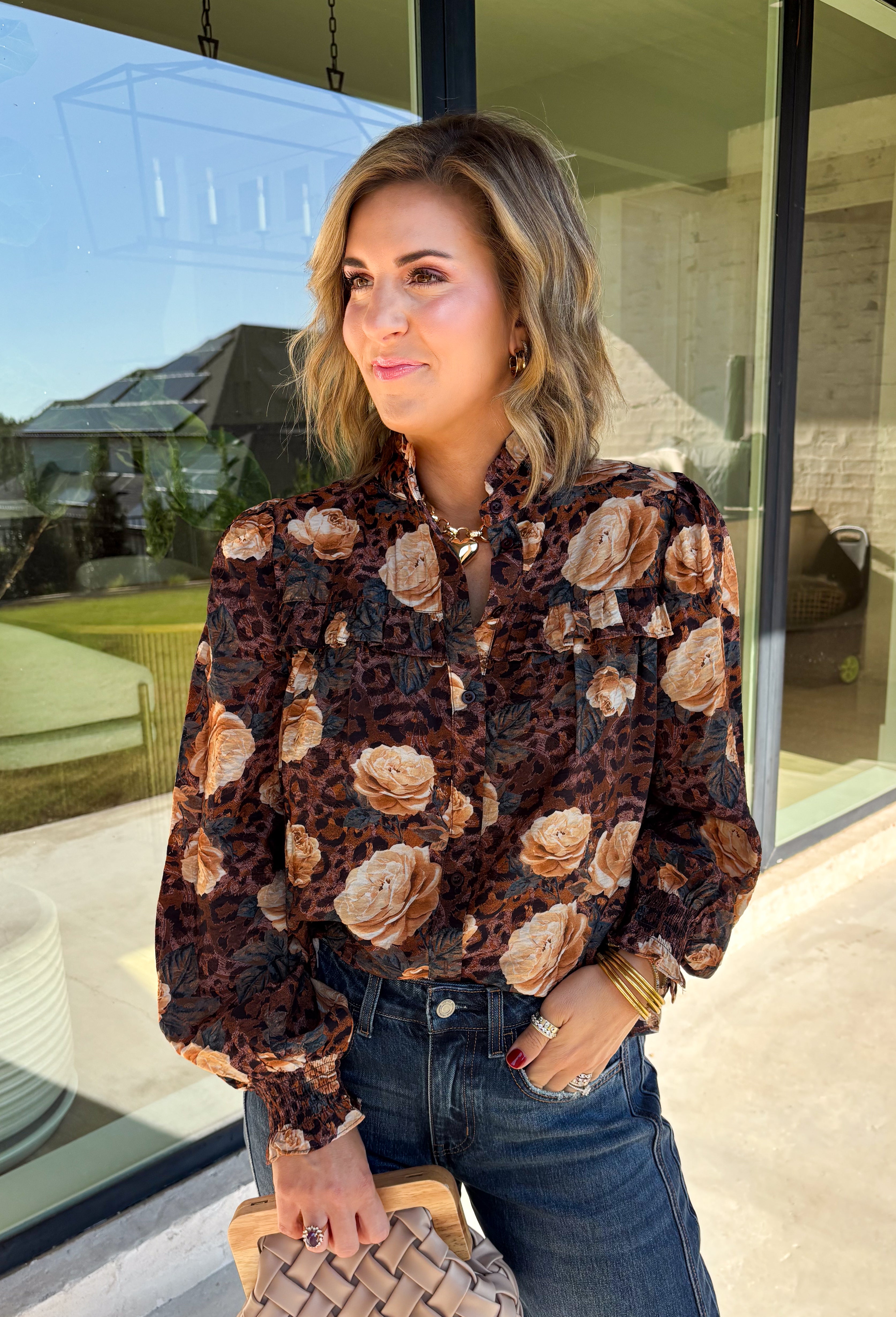Bring a fresh twist to your fall wardrobe with this beautifully detailed blouse from Fate. Featuring a rich brown leopard-inspired print accented with a soft neutral floral design, this feminine top effortlessly blends bold style with timeless charm. The button-front silhouette is finished with a subtle ruffle neckline and delicate ruffle details throughout the front and back for added texture. 