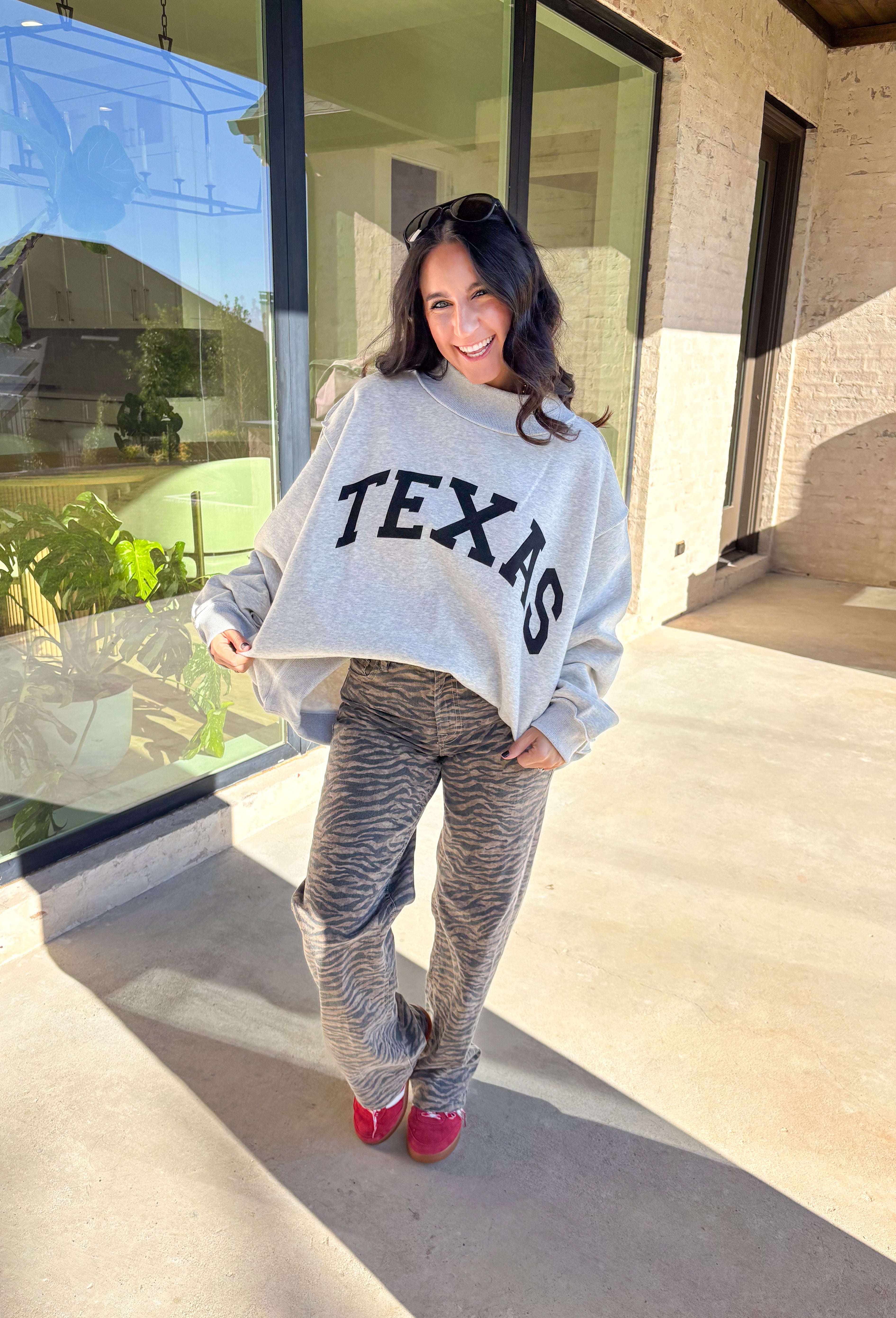 Show your Lone Star pride in this cozy reversible pullover by Bucket List! Crafted from soft fleece, this heather gray mock neck sweatshirt offers two fun looks in one—one side reads “Texas” in bold black lettering, while the reverse features “TX” in bright hot pink. Warm, comfy, and effortlessly cool, it’s perfect for everything from game days to laid-back weekends.