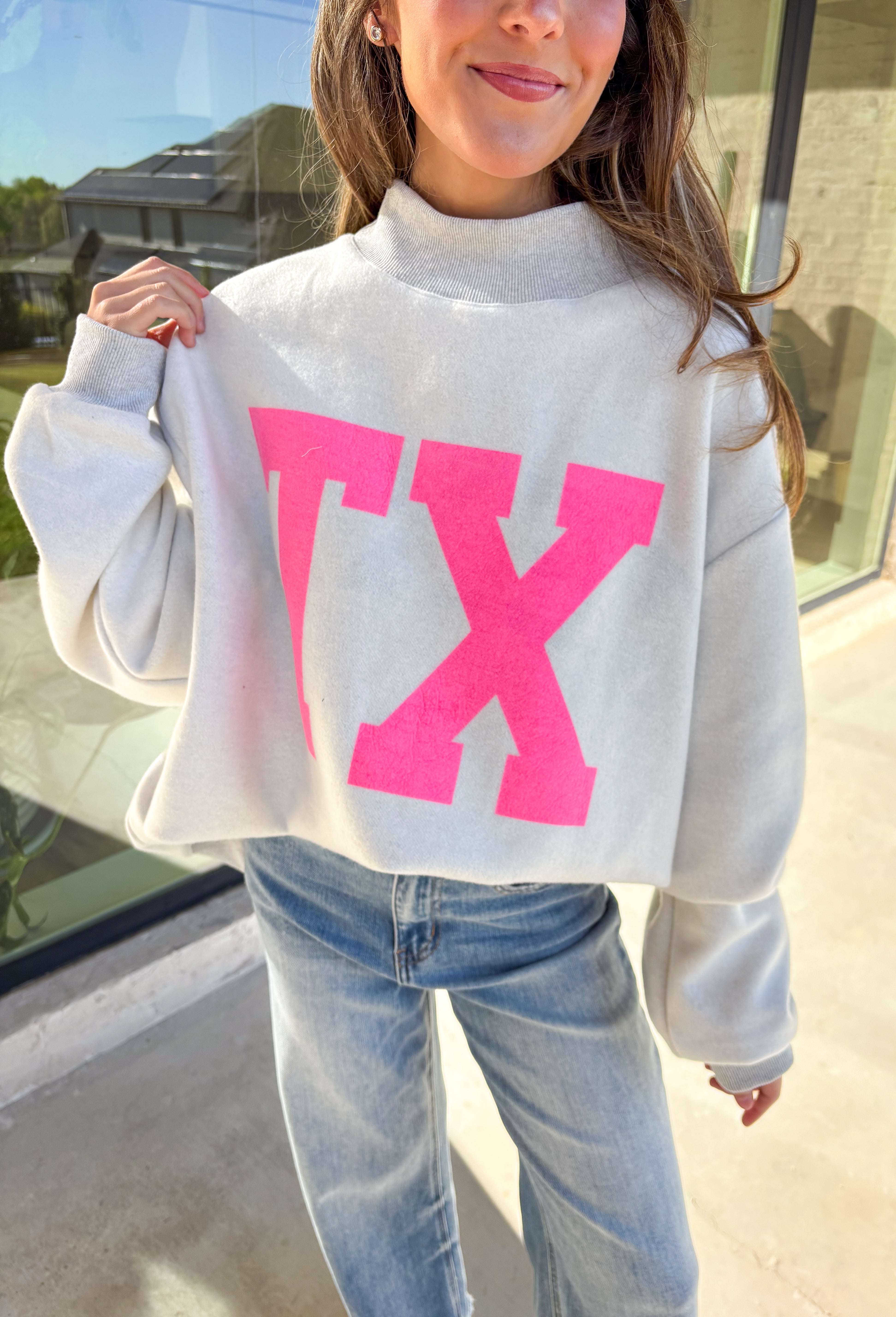 Show your Lone Star pride in this cozy reversible pullover by Bucket List! Crafted from soft fleece, this heather gray mock neck sweatshirt offers two fun looks in one—one side reads “Texas” in bold black lettering, while the reverse features “TX” in bright hot pink. Warm, comfy, and effortlessly cool, it’s perfect for everything from game days to laid-back weekends.