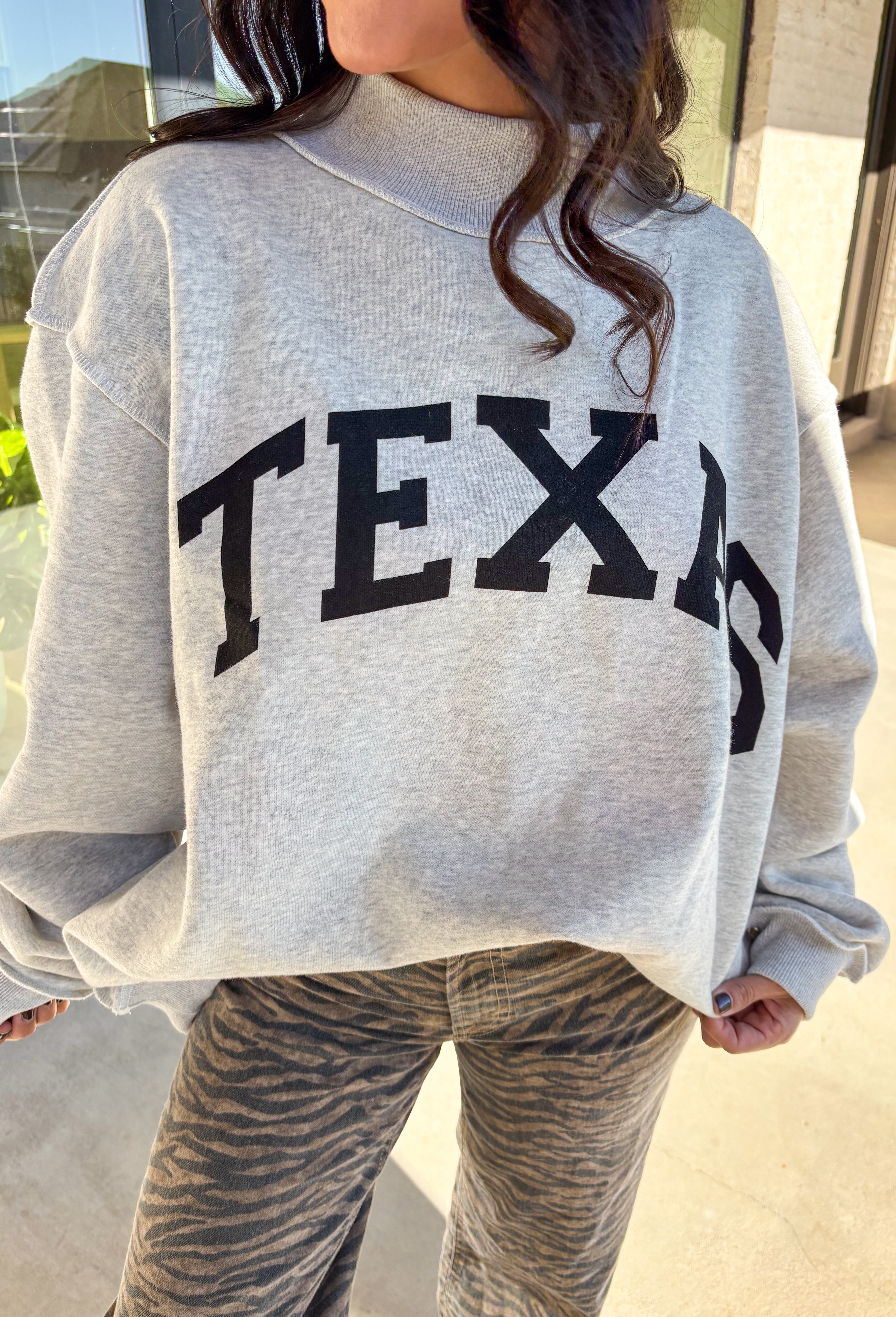 Show your Lone Star pride in this cozy reversible pullover by Bucket List! Crafted from soft fleece, this heather gray mock neck sweatshirt offers two fun looks in one—one side reads “Texas” in bold black lettering, while the reverse features “TX” in bright hot pink. Warm, comfy, and effortlessly cool, it’s perfect for everything from game days to laid-back weekends.