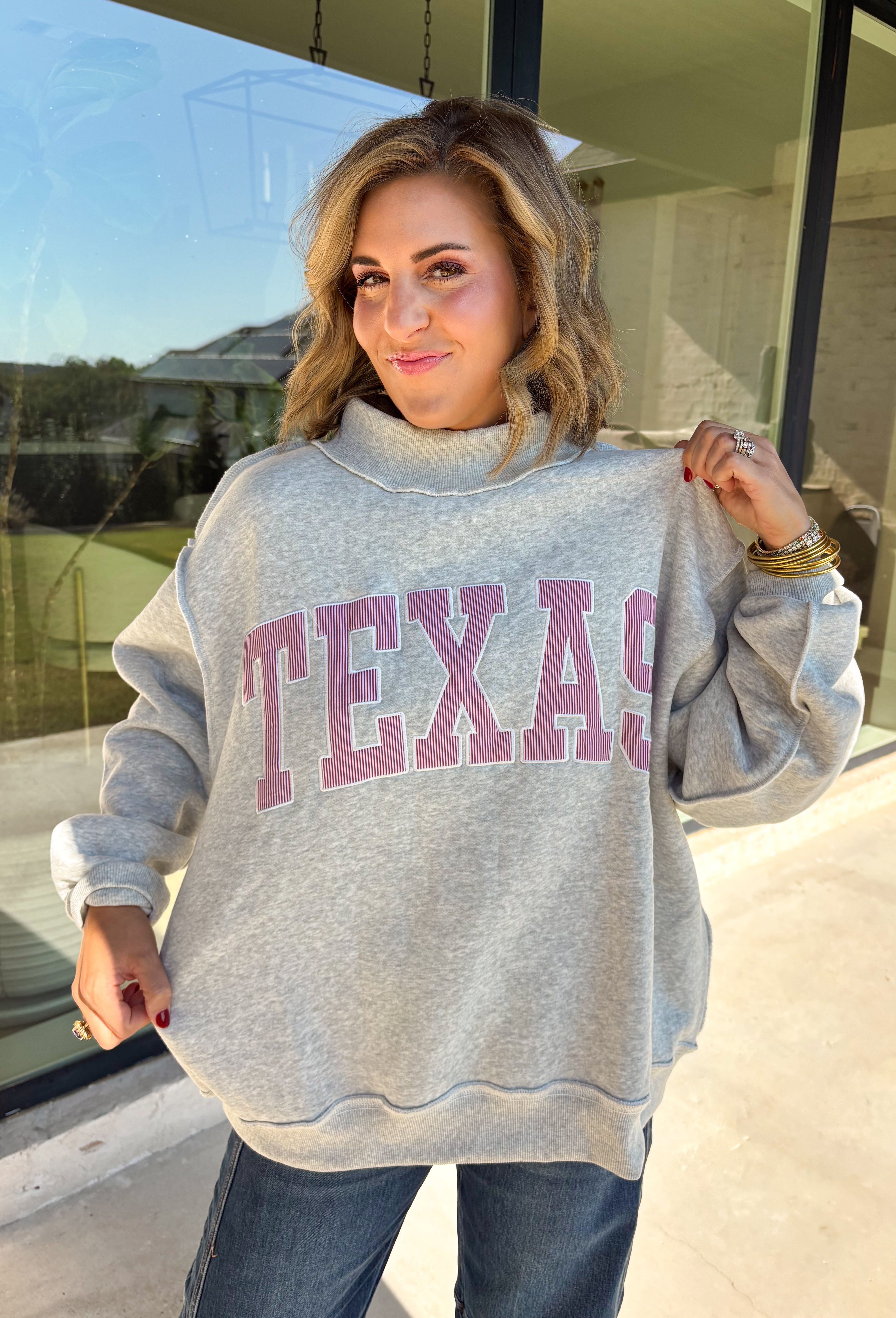 Show a little Lone Star love while staying extra cozy in this heather grey “Texas” pullover from Bucket List. The bold lettering features a crimson and white stripe print, with each letter outlined in white embroidery for added texture and a standout finish. A mock neckline and long sleeves give it a cozy cold-weather feel, while the fleece-lined interior makes it perfect for crisp fall mornings and chilly weekends. 