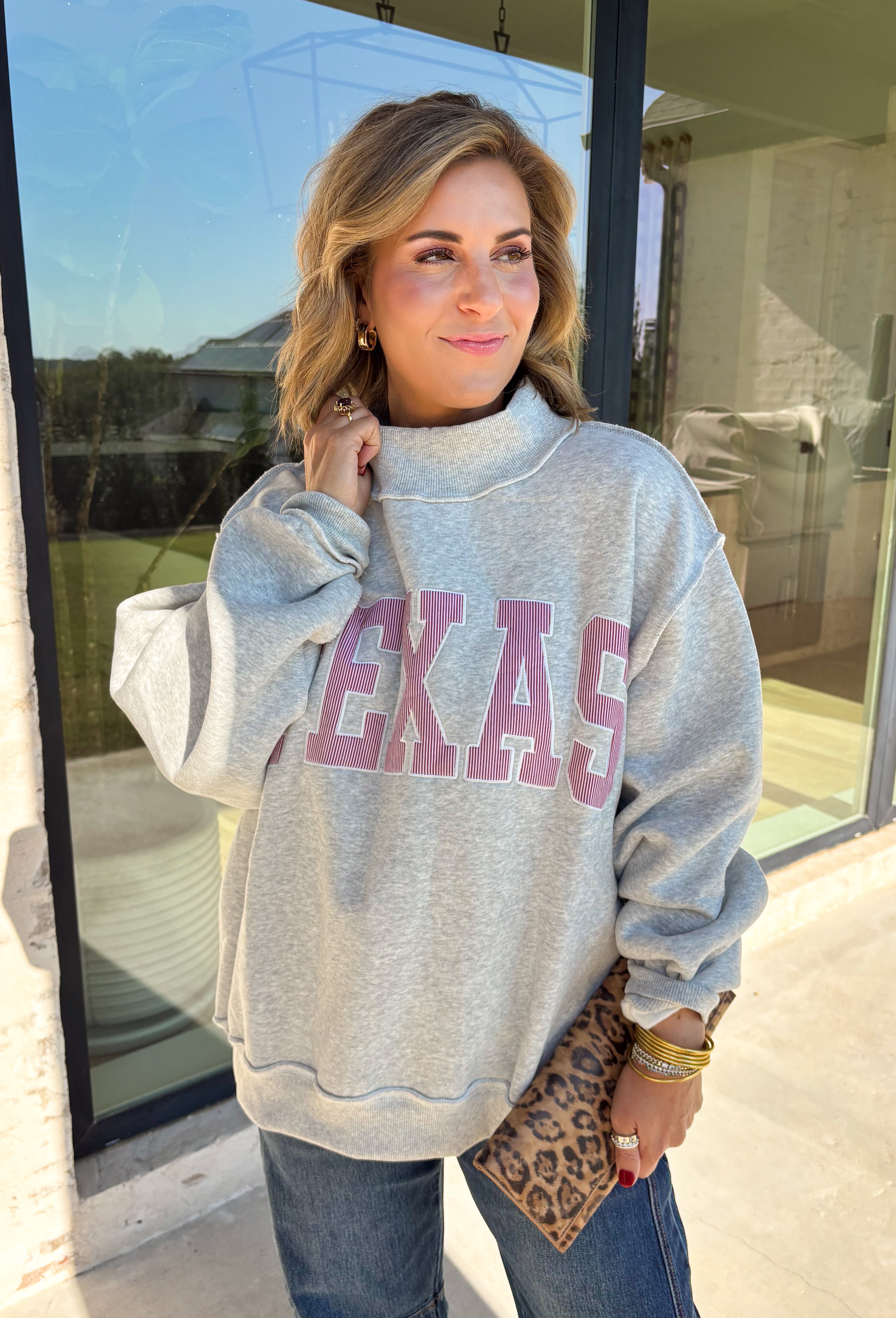 Show a little Lone Star love while staying extra cozy in this heather grey “Texas” pullover from Bucket List. The bold lettering features a crimson and white stripe print, with each letter outlined in white embroidery for added texture and a standout finish. A mock neckline and long sleeves give it a cozy cold-weather feel, while the fleece-lined interior makes it perfect for crisp fall mornings and chilly weekends. 