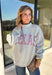 Show a little Lone Star love while staying extra cozy in this heather grey “Texas” pullover from Bucket List. The bold lettering features a crimson and white stripe print, with each letter outlined in white embroidery for added texture and a standout finish. A mock neckline and long sleeves give it a cozy cold-weather feel, while the fleece-lined interior makes it perfect for crisp fall mornings and chilly weekends. 