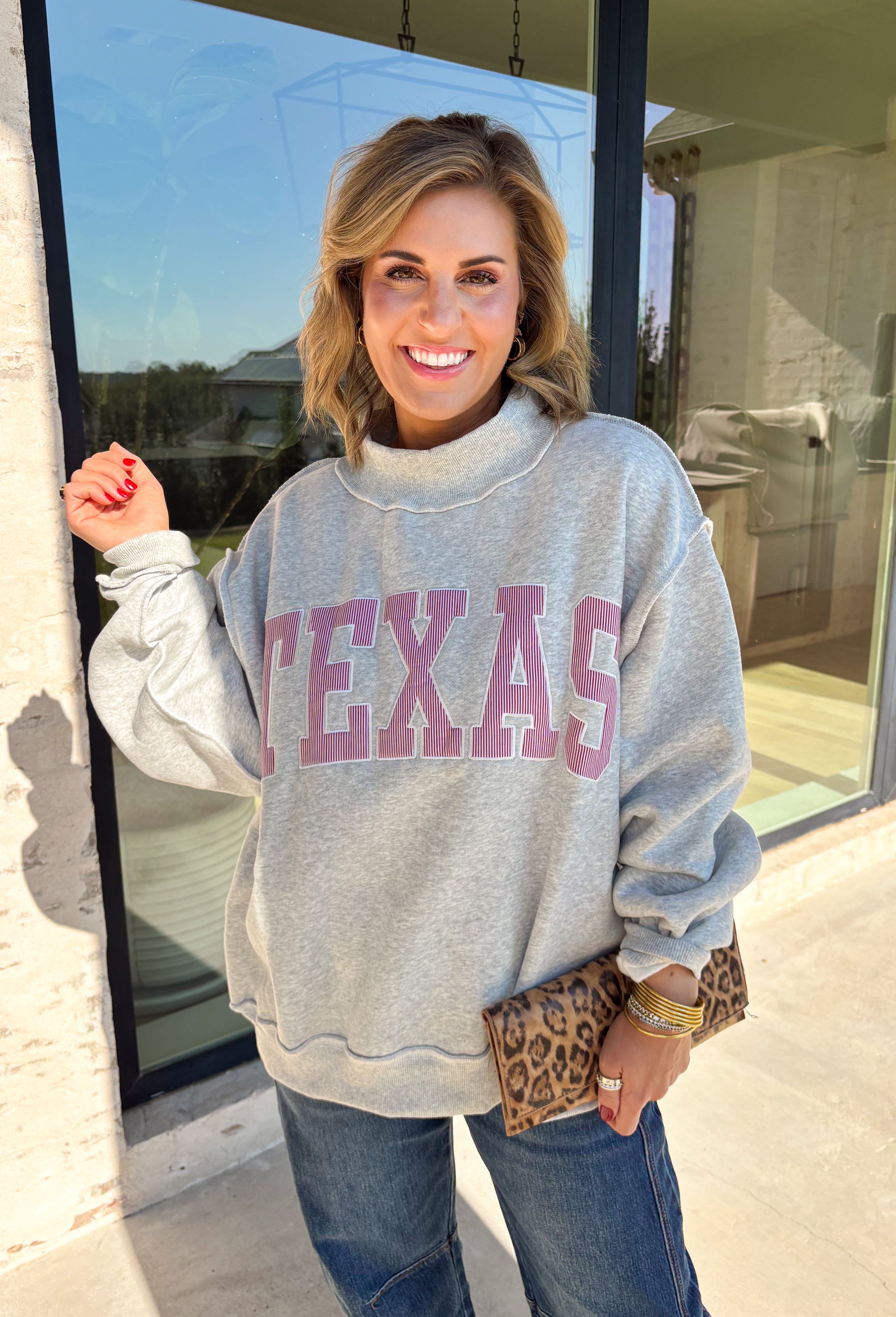 Show a little Lone Star love while staying extra cozy in this heather grey “Texas” pullover from Bucket List. The bold lettering features a crimson and white stripe print, with each letter outlined in white embroidery for added texture and a standout finish. A mock neckline and long sleeves give it a cozy cold-weather feel, while the fleece-lined interior makes it perfect for crisp fall mornings and chilly weekends. 