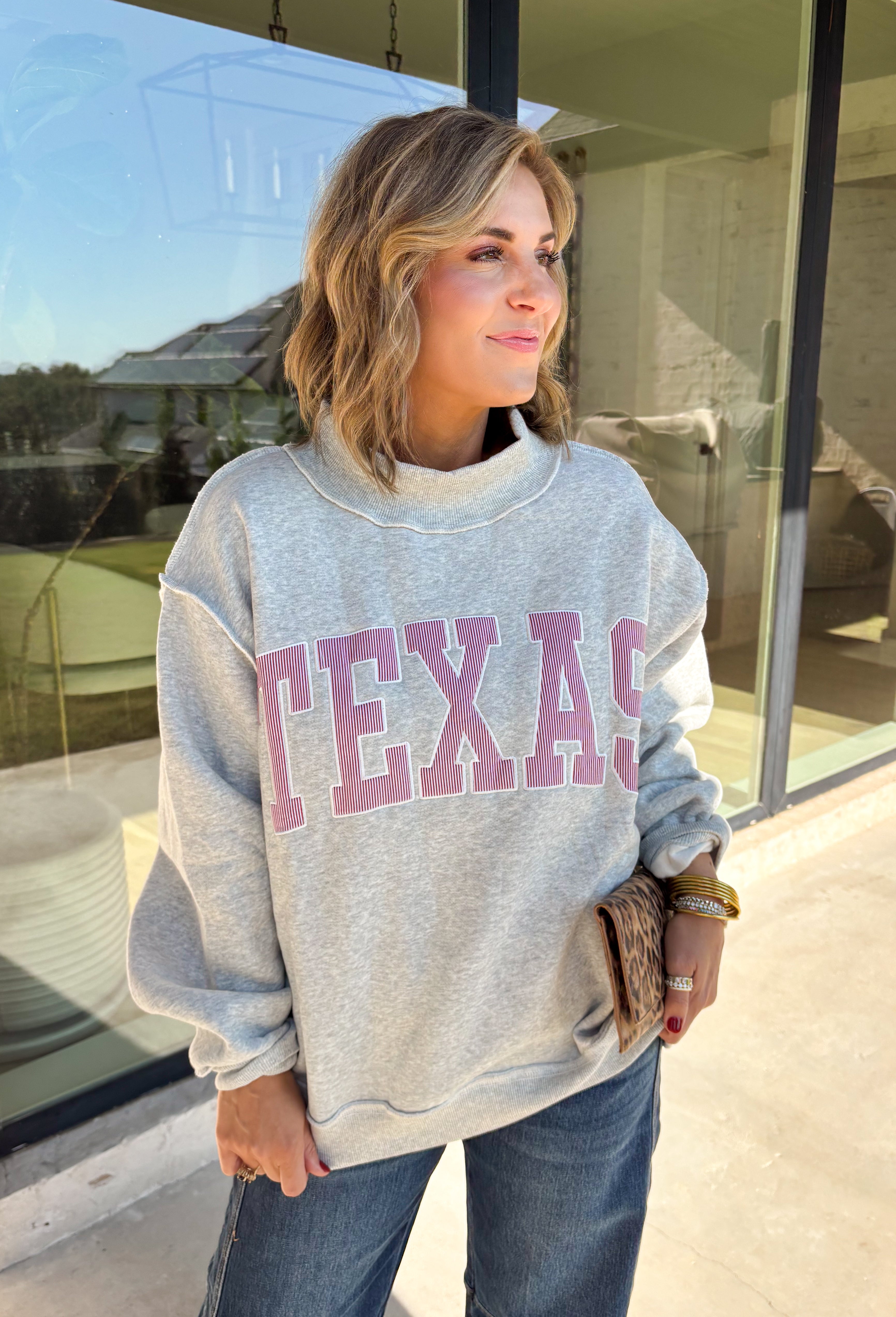 Show a little Lone Star love while staying extra cozy in this heather grey “Texas” pullover from Bucket List. The bold lettering features a crimson and white stripe print, with each letter outlined in white embroidery for added texture and a standout finish. A mock neckline and long sleeves give it a cozy cold-weather feel, while the fleece-lined interior makes it perfect for crisp fall mornings and chilly weekends. 