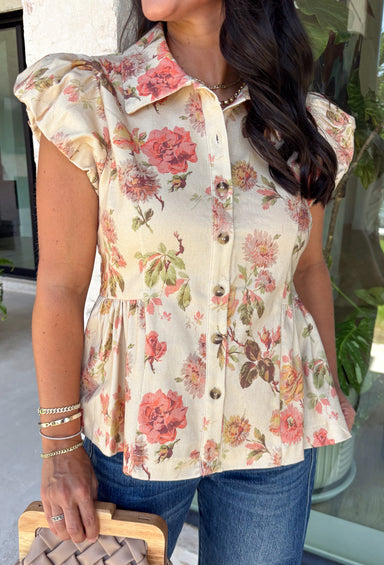 Fresh florals meet cozy fall style in this charming peplum blouse. Featuring a soft neutral backdrop with delicate pops of pink and green, this top brings just the right amount of color to your autumn wardrobe. The collared neckline and button front add a timeless, polished touch, while the peplum hem creates a flattering silhouette you'll love. Elastic puff sleeves complete the look with feminine charm, making this top perfect for everything from workdays to weekend brunches.