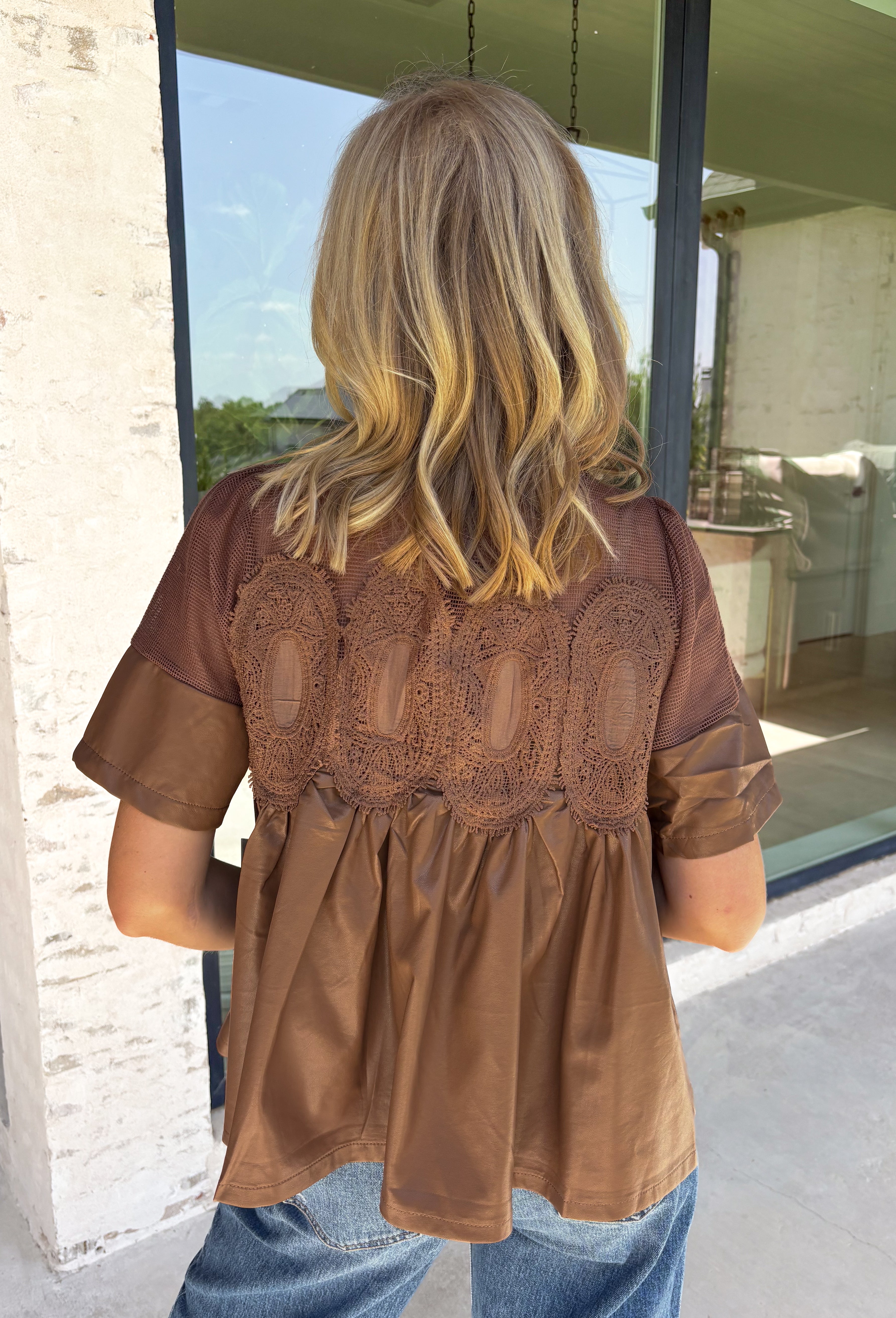 Elevate your fall wardrobe with this stunning faux leather top that perfectly blends edgy style with feminine charm. Designed in a rich chocolate brown, this statement piece features beautiful lace detailing along the front that softens the sleek faux leather finish for a look that's effortlessly sophisticated. The textured fabric adds depth and dimension, while the classic short sleeve silhouette makes it easy to style from season to season. 