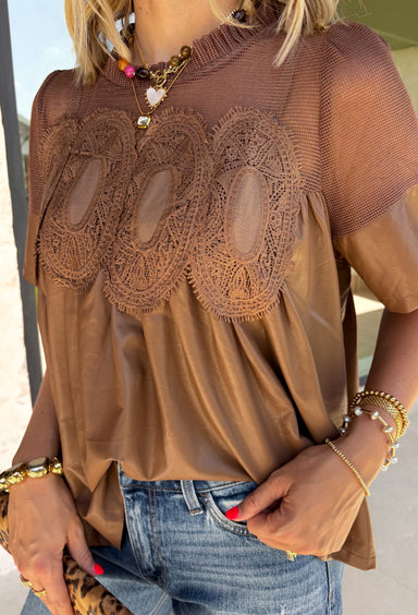 Elevate your fall wardrobe with this stunning faux leather top that perfectly blends edgy style with feminine charm. Designed in a rich chocolate brown, this statement piece features beautiful lace detailing along the front that softens the sleek faux leather finish for a look that's effortlessly sophisticated. The textured fabric adds depth and dimension, while the classic short sleeve silhouette makes it easy to style from season to season. 