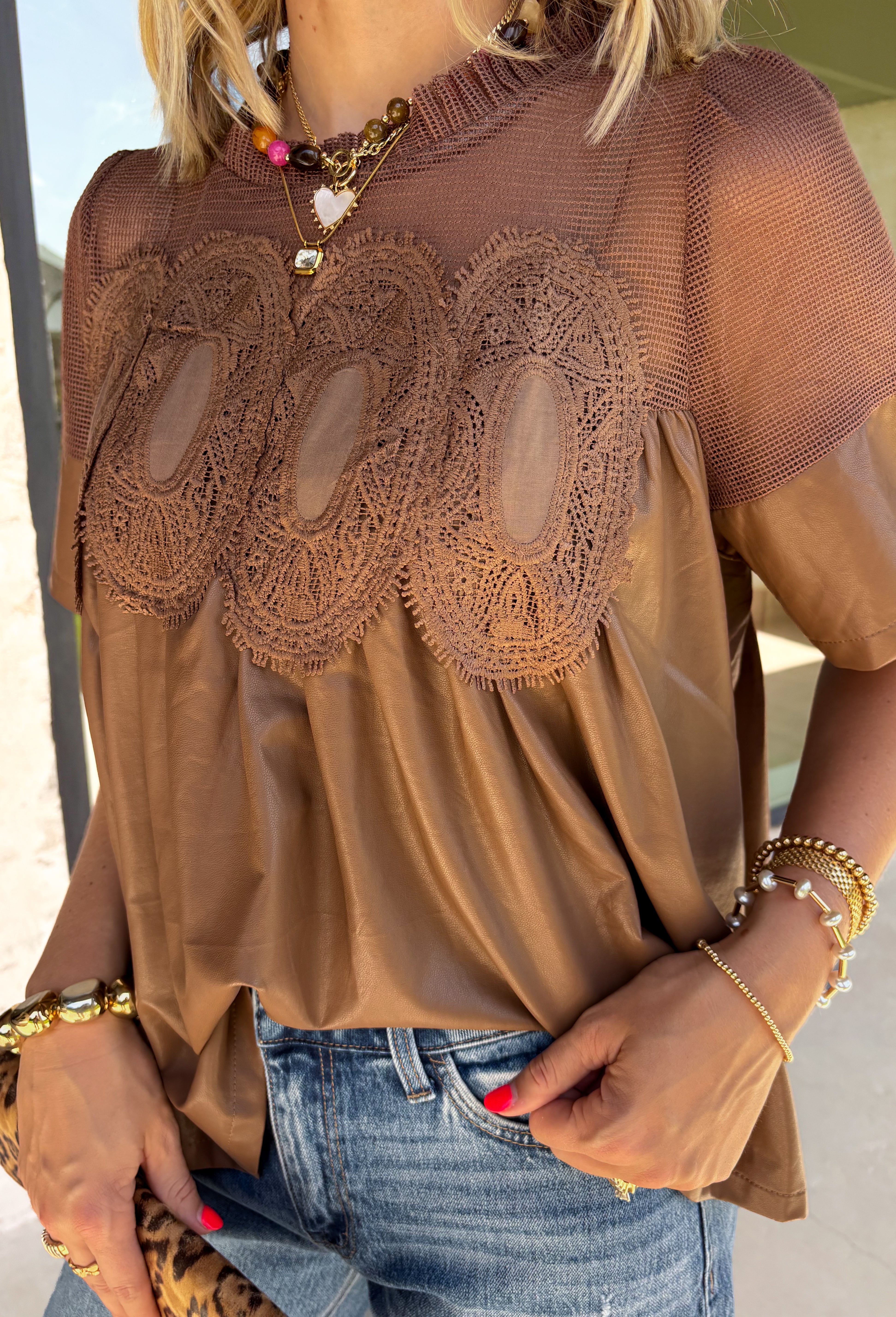 Elevate your fall wardrobe with this stunning faux leather top that perfectly blends edgy style with feminine charm. Designed in a rich chocolate brown, this statement piece features beautiful lace detailing along the front that softens the sleek faux leather finish for a look that's effortlessly sophisticated. The textured fabric adds depth and dimension, while the classic short sleeve silhouette makes it easy to style from season to season. 