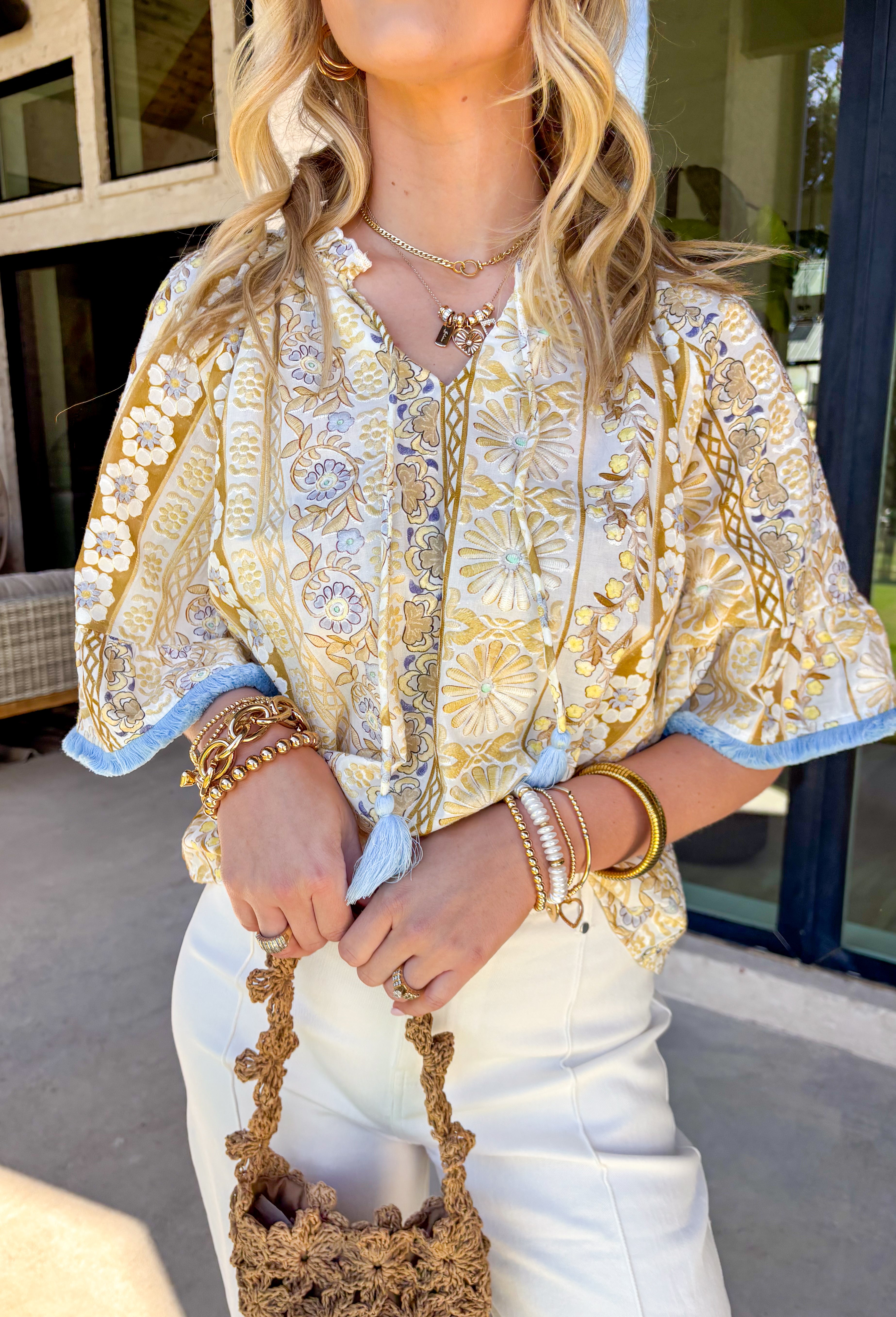 This sweet little spring top is basically sunshine in outfit form! Featuring a crisp white base with soft yellow florals and the prettiest hints of baby blue, it’s the kind of piece that instantly brightens your day. The subtle ruffle neckline keeps it feminine and fun, while the front tie with tassel details adds that effortless “threw it on and still look cute” vibe. 
