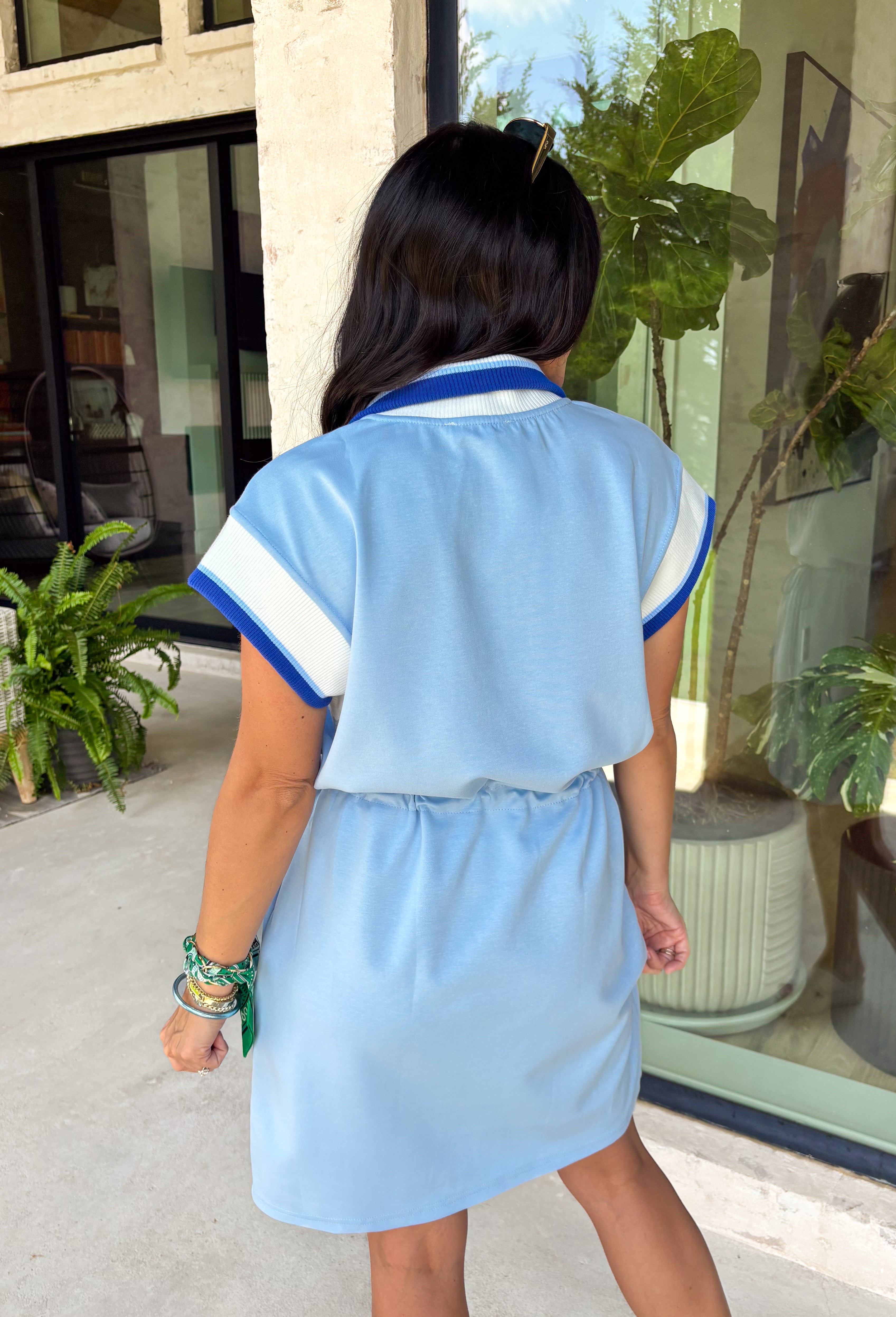 This light blue short sleeve dress is the perfect mix of sporty and cute for summer! Designed with a quarter zip neckline and elastic self-tie waist, it gives you that flattering, adjustable fit while keeping things comfortable for all-day wear. The navy, light blue, and white athletic stripe detail along the front, neckline, and cuffs adds a fun, energetic touch that makes this one stand out. Finished with side pockets (always a win), it’s perfect for everything from errands to casual plans. 