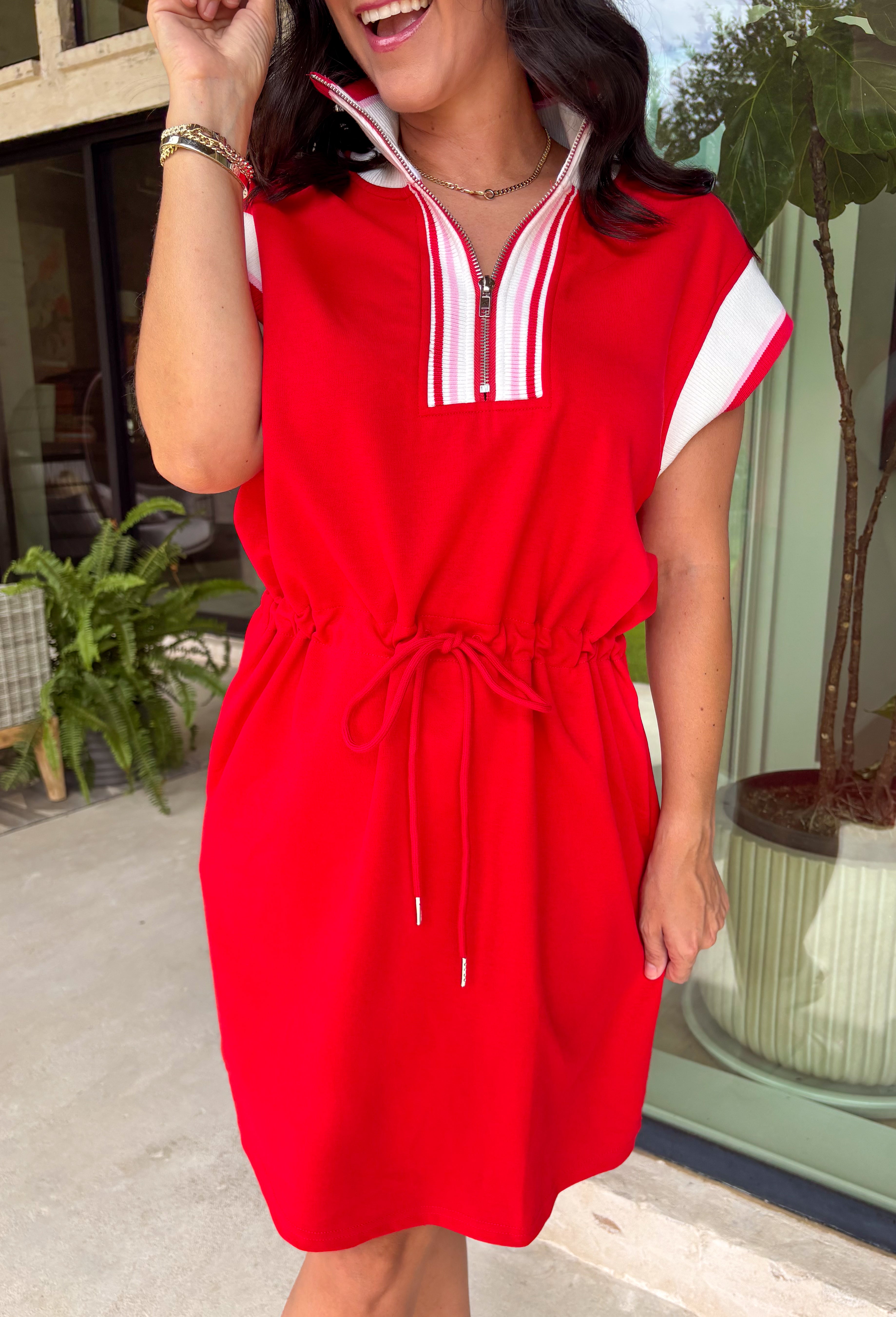 This red short sleeve dress is the perfect mix of sporty and cute for summer! Designed with a quarter zip neckline and elastic self-tie waist, it gives you that flattering, adjustable fit while keeping things comfortable for all-day wear. The red, pink, and white athletic stripe detail along the front, neckline, and cuffs adds a fun, energetic touch that makes this one stand out. Finished with side pockets (always a win), it’s perfect for everything from errands to casual plans.