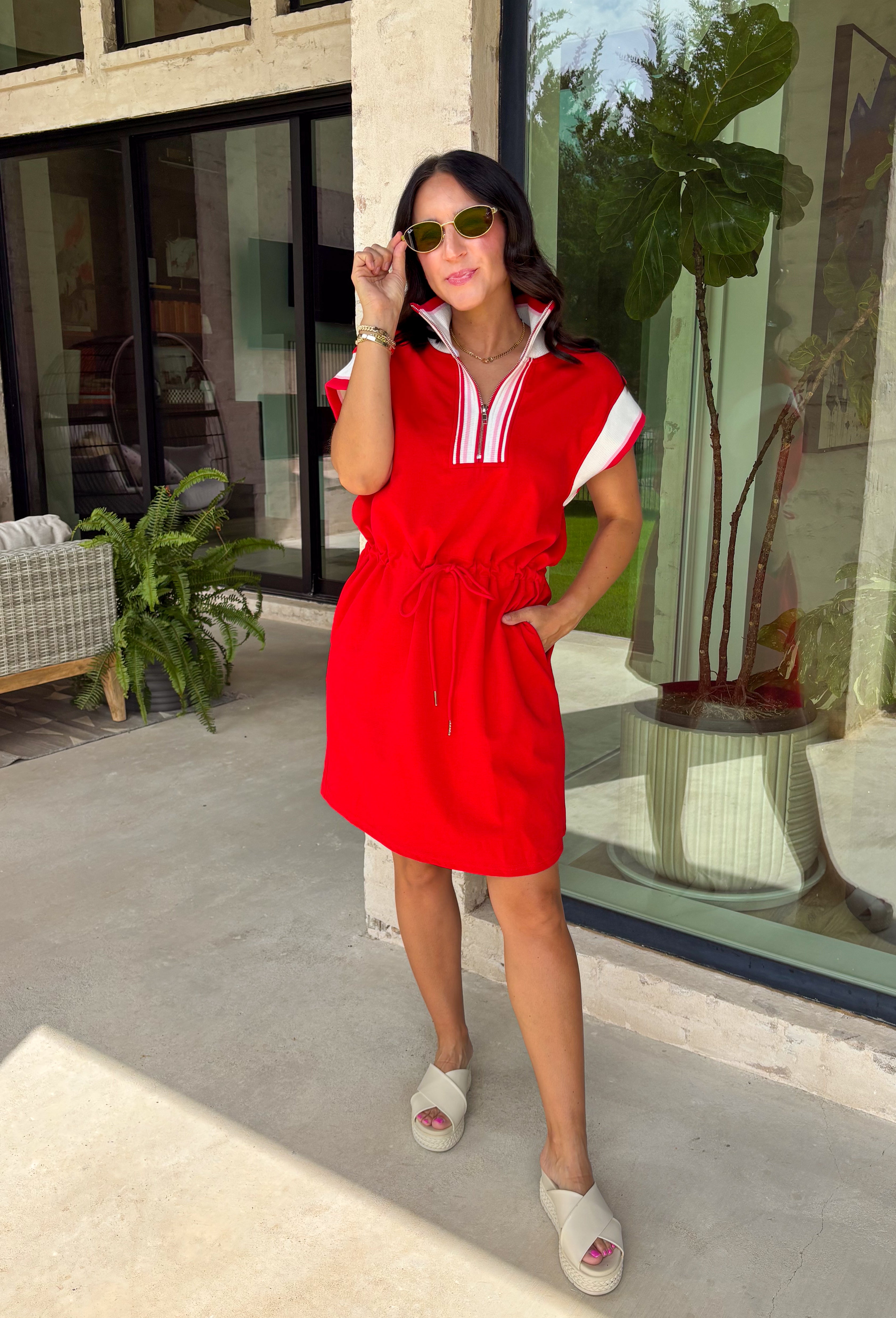 This red short sleeve dress is the perfect mix of sporty and cute for summer! Designed with a quarter zip neckline and elastic self-tie waist, it gives you that flattering, adjustable fit while keeping things comfortable for all-day wear. The red, pink, and white athletic stripe detail along the front, neckline, and cuffs adds a fun, energetic touch that makes this one stand out. Finished with side pockets (always a win), it’s perfect for everything from errands to casual plans.