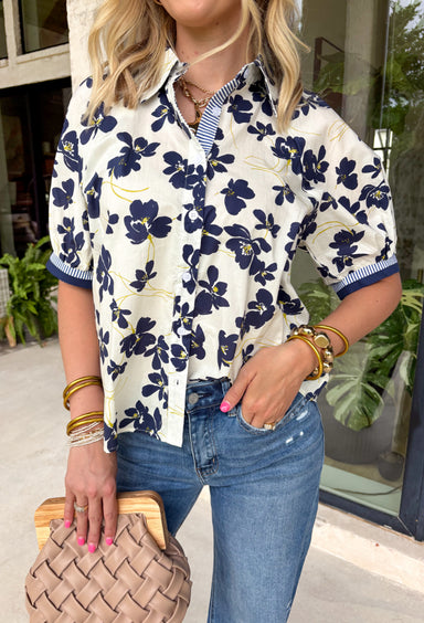 This off white floral top is the perfect transition piece for fall days! The navy floral print with subtle hints of green brings in those rich, seasonal tones while still feeling light and easy to wear. The collared neckline and button down front give it a polished feel, while the navy and white stripe detail along the front and sleeves adds a fun, unexpected touch. Made from breathable cotton, it’s perfect for layering now and wearing into cooler days.