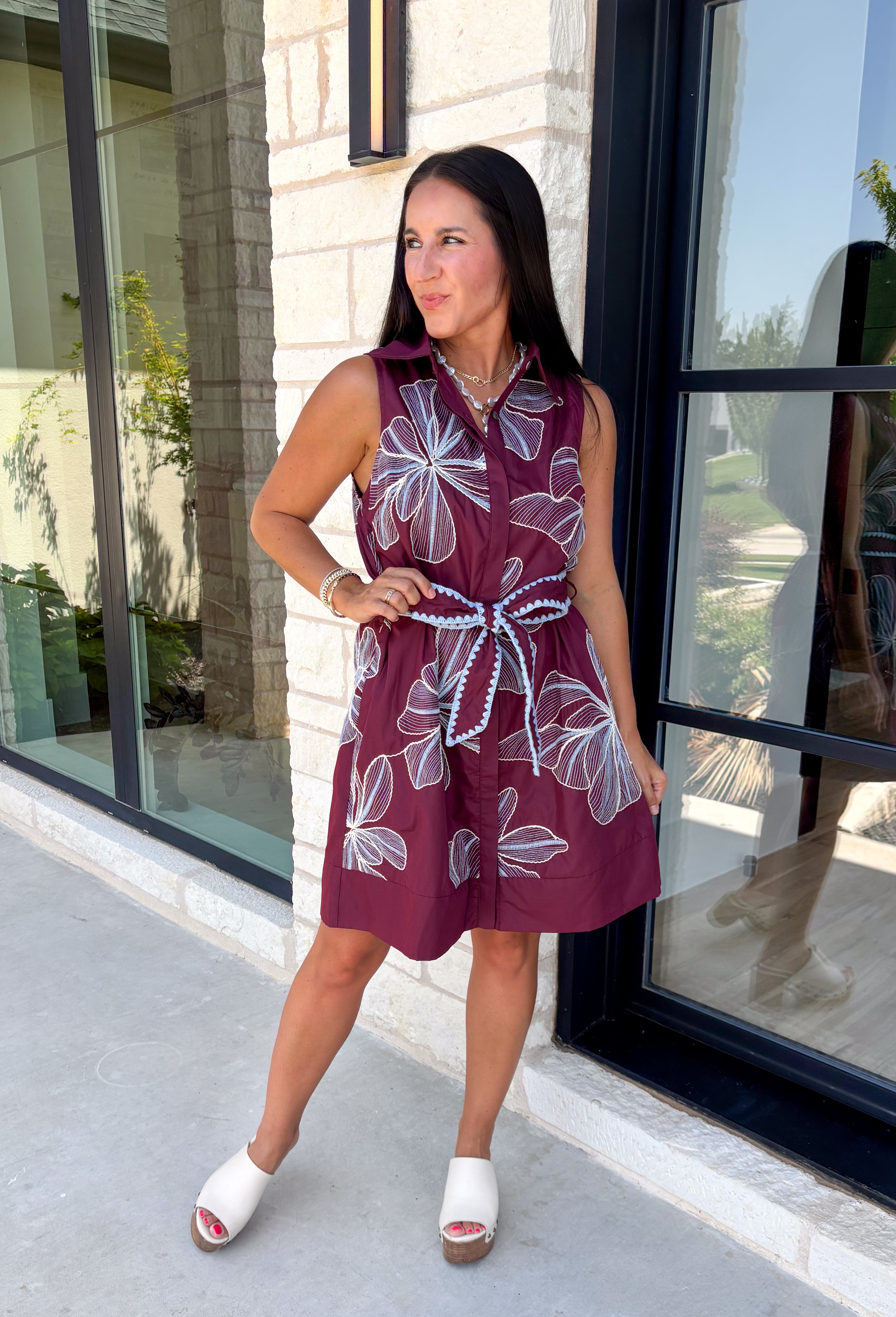 Rich fall colors and beautiful embroidered details make this dress an instant seasonal favorite! Crafted in a gorgeous wine hue, this sleeveless dress features delicate light blue and off white floral embroidery that creates a charming, handcrafted look. The button front and self-tie waist belt with playful contrast pom trim create a flattering silhouette, while side pockets and a fully lined design make it as practical as it is beautiful. 