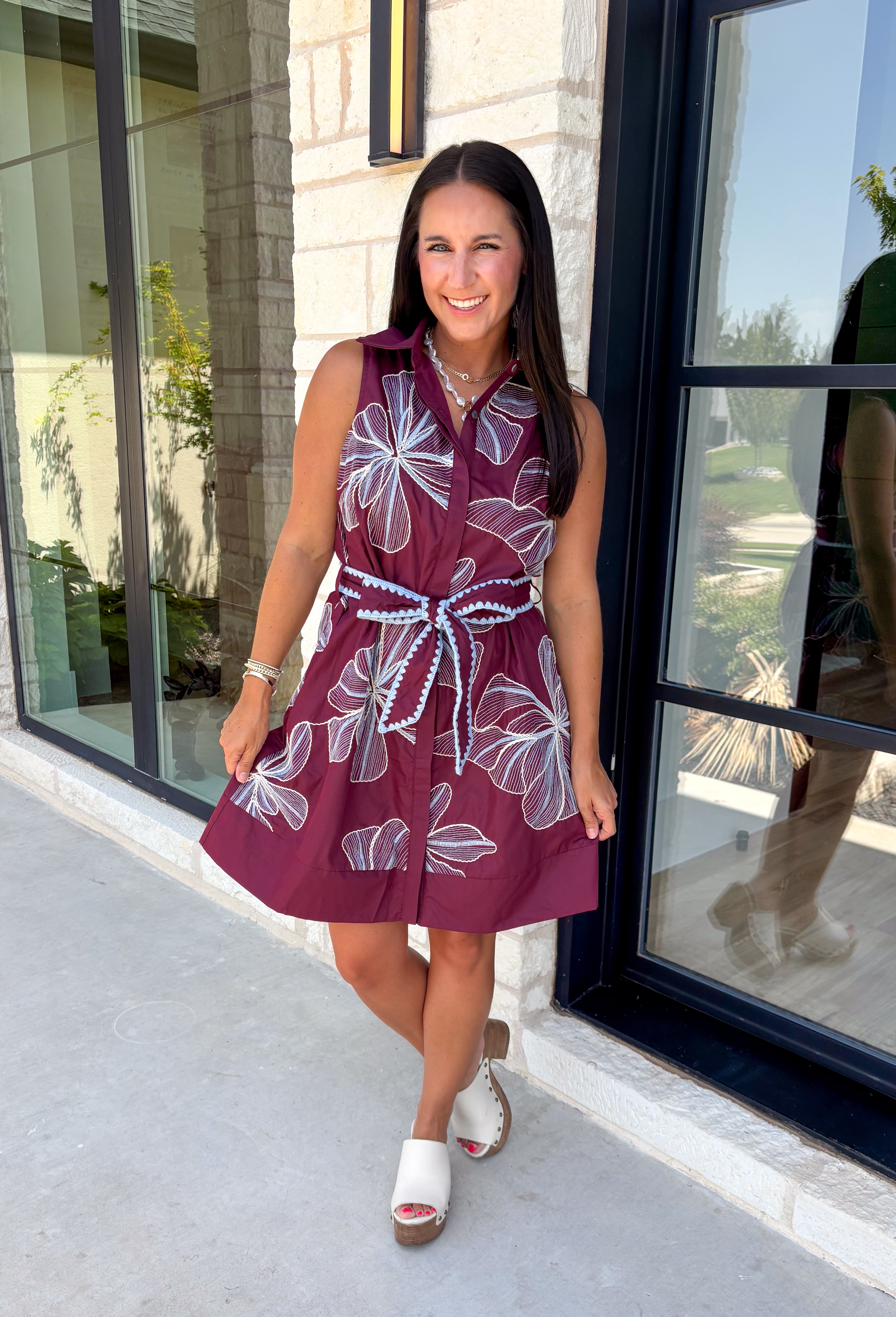 Rich fall colors and beautiful embroidered details make this dress an instant seasonal favorite! Crafted in a gorgeous wine hue, this sleeveless dress features delicate light blue and off white floral embroidery that creates a charming, handcrafted look. The button front and self-tie waist belt with playful contrast pom trim create a flattering silhouette, while side pockets and a fully lined design make it as practical as it is beautiful. 