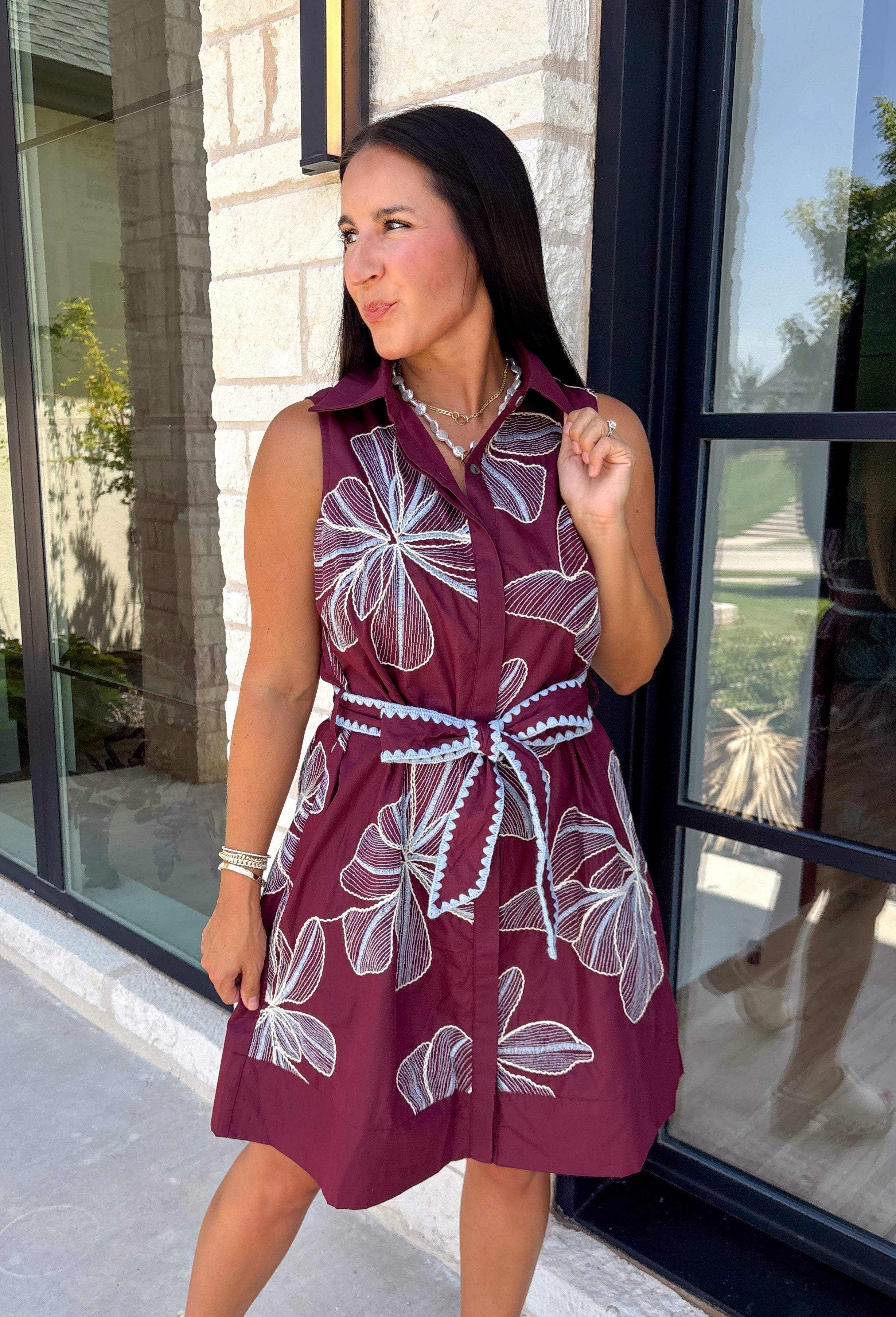 Rich fall colors and beautiful embroidered details make this dress an instant seasonal favorite! Crafted in a gorgeous wine hue, this sleeveless dress features delicate light blue and off white floral embroidery that creates a charming, handcrafted look. The button front and self-tie waist belt with playful contrast pom trim create a flattering silhouette, while side pockets and a fully lined design make it as practical as it is beautiful. 