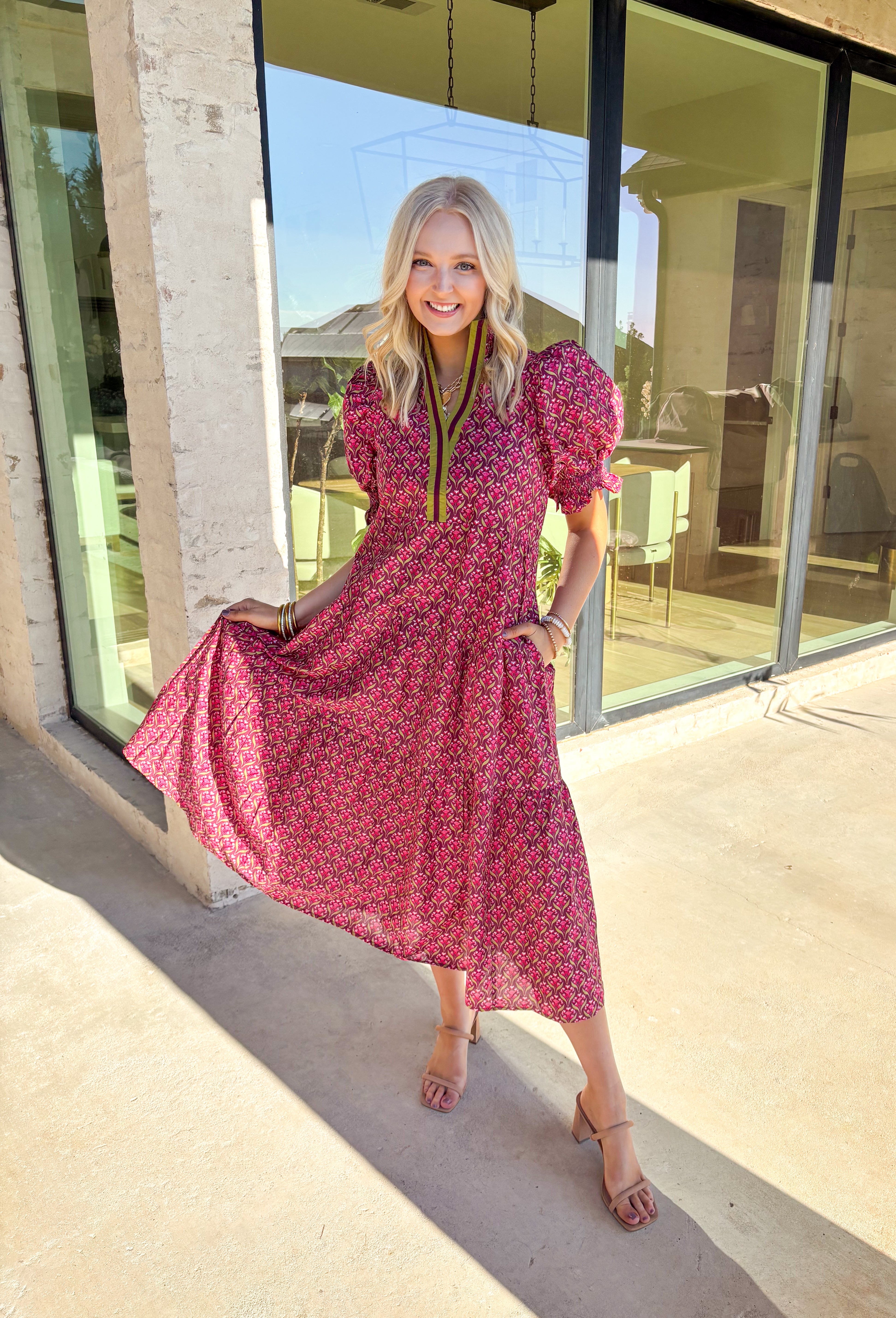 Romantic florals meet effortless style in this puff sleeve midi dress by Entro. Set against a rich burgundy background, the botanical print features shades of pink with subtle pops of olive for a seasonal feel. A split neckline trimmed in contrast detailing adds a polished touch, while smocked cuffs and a smocked collar bring in texture and comfort. Side pockets and a full lining make this dress as practical as it is beautiful, perfect for everything from special occasions to fall gatherings.