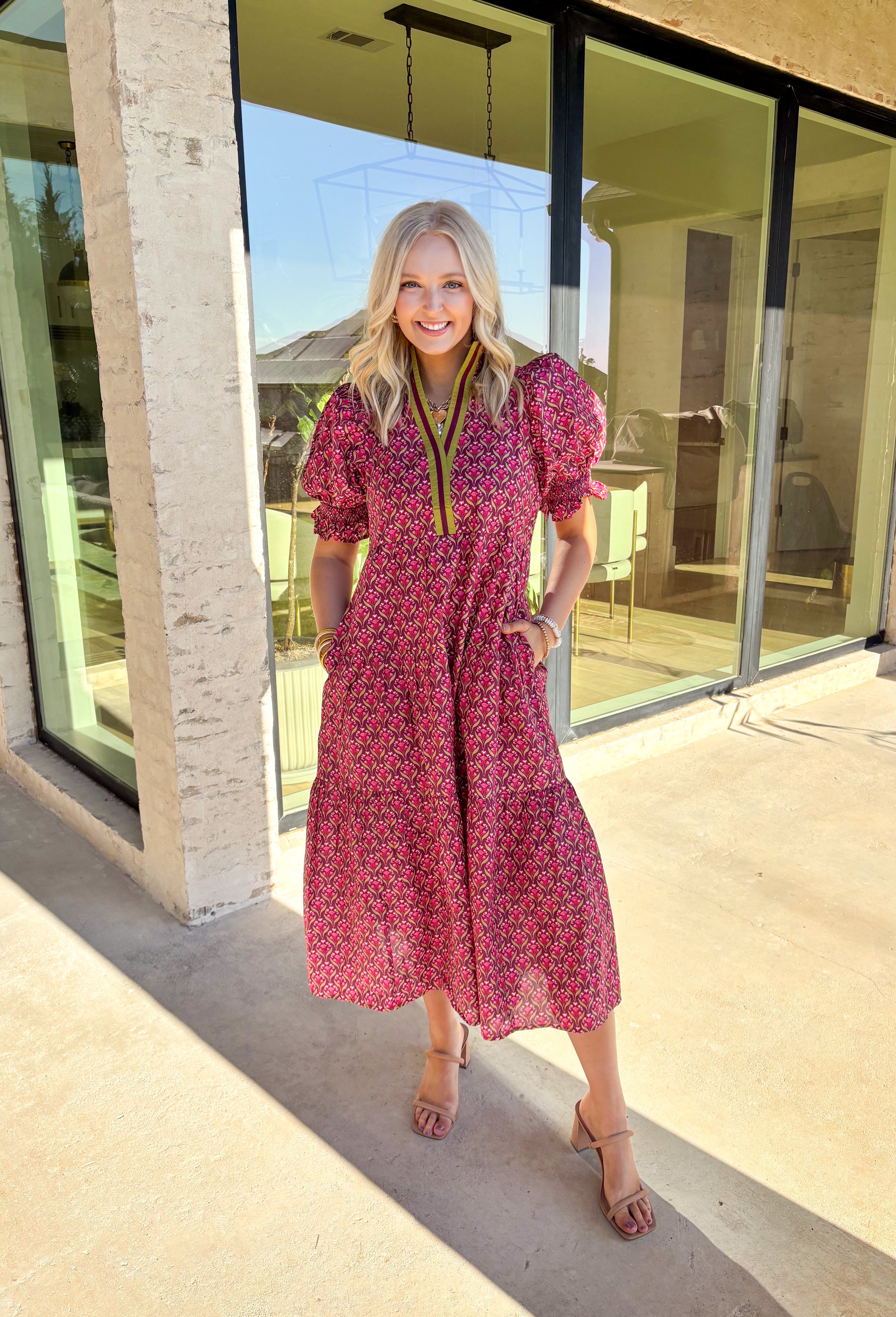 Romantic florals meet effortless style in this puff sleeve midi dress by Entro. Set against a rich burgundy background, the botanical print features shades of pink with subtle pops of olive for a seasonal feel. A split neckline trimmed in contrast detailing adds a polished touch, while smocked cuffs and a smocked collar bring in texture and comfort. Side pockets and a full lining make this dress as practical as it is beautiful, perfect for everything from special occasions to fall gatherings.