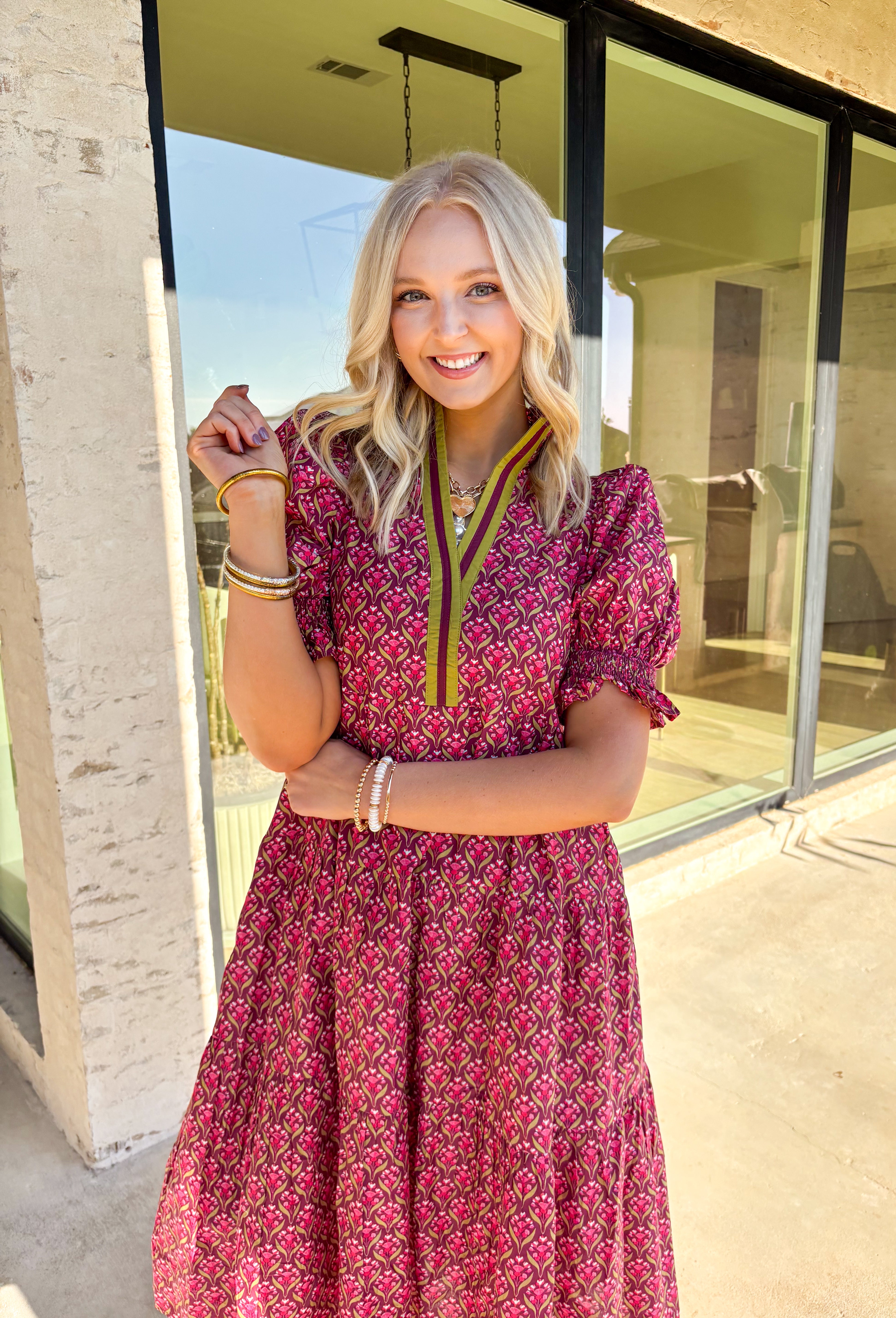Romantic florals meet effortless style in this puff sleeve midi dress by Entro. Set against a rich burgundy background, the botanical print features shades of pink with subtle pops of olive for a seasonal feel. A split neckline trimmed in contrast detailing adds a polished touch, while smocked cuffs and a smocked collar bring in texture and comfort. Side pockets and a full lining make this dress as practical as it is beautiful, perfect for everything from special occasions to fall gatherings.