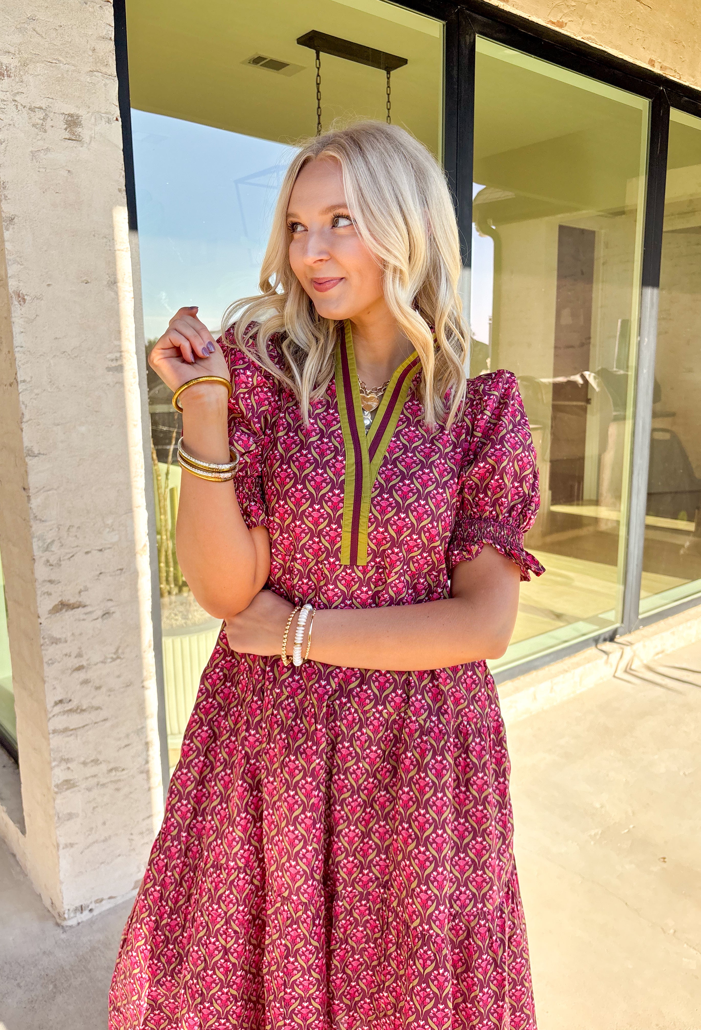Romantic florals meet effortless style in this puff sleeve midi dress by Entro. Set against a rich burgundy background, the botanical print features shades of pink with subtle pops of olive for a seasonal feel. A split neckline trimmed in contrast detailing adds a polished touch, while smocked cuffs and a smocked collar bring in texture and comfort. Side pockets and a full lining make this dress as practical as it is beautiful, perfect for everything from special occasions to fall gatherings.