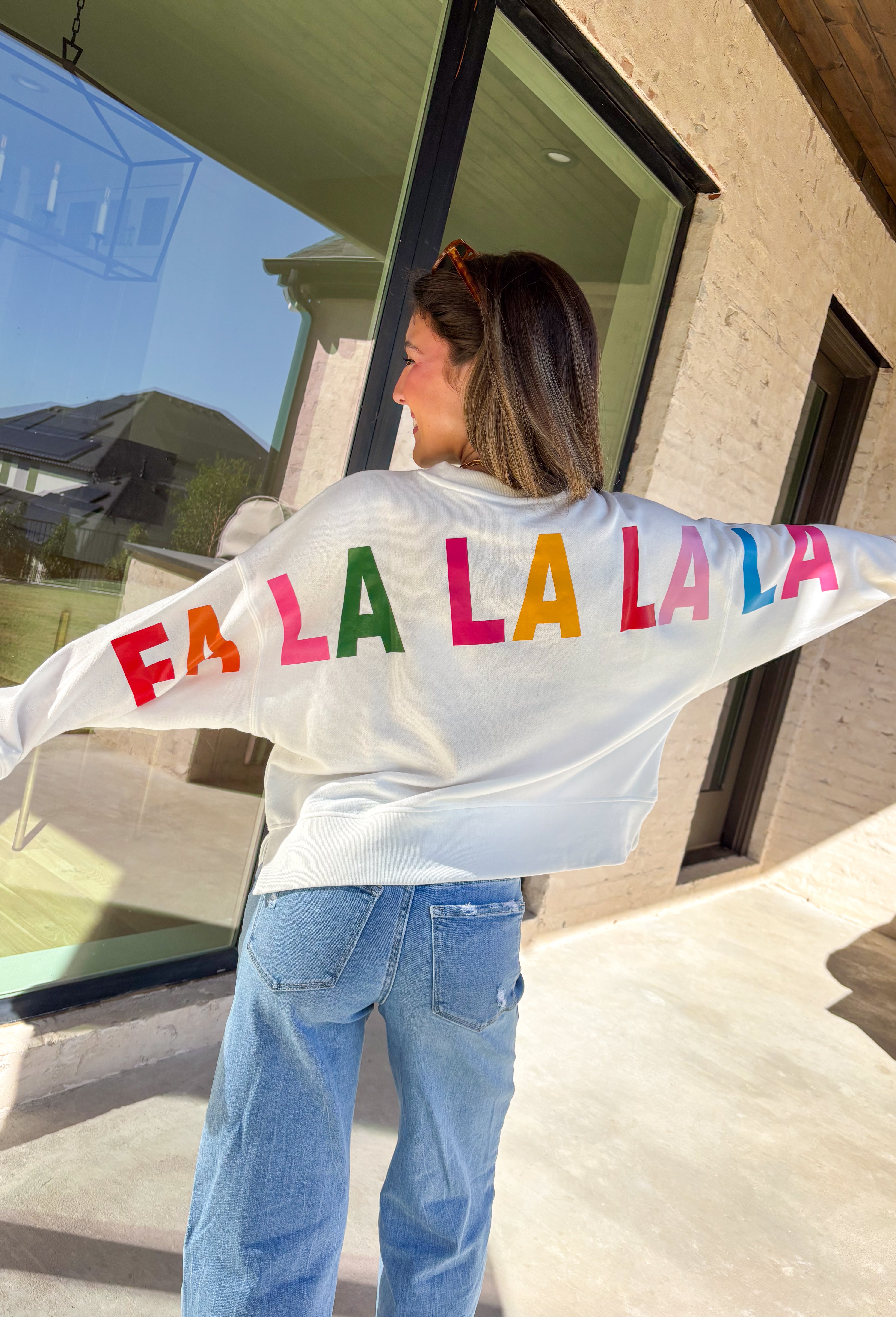 Get in the holiday spirit with this cheerful white pullover by Shiraleah! The front features a textured red “‘Tis The Season” design, while the back adds a playful surprise with a colorful “Fa La La” print. Its soft fabric and cropped fit make it the perfect piece for decking the halls or cozy nights by the fire.