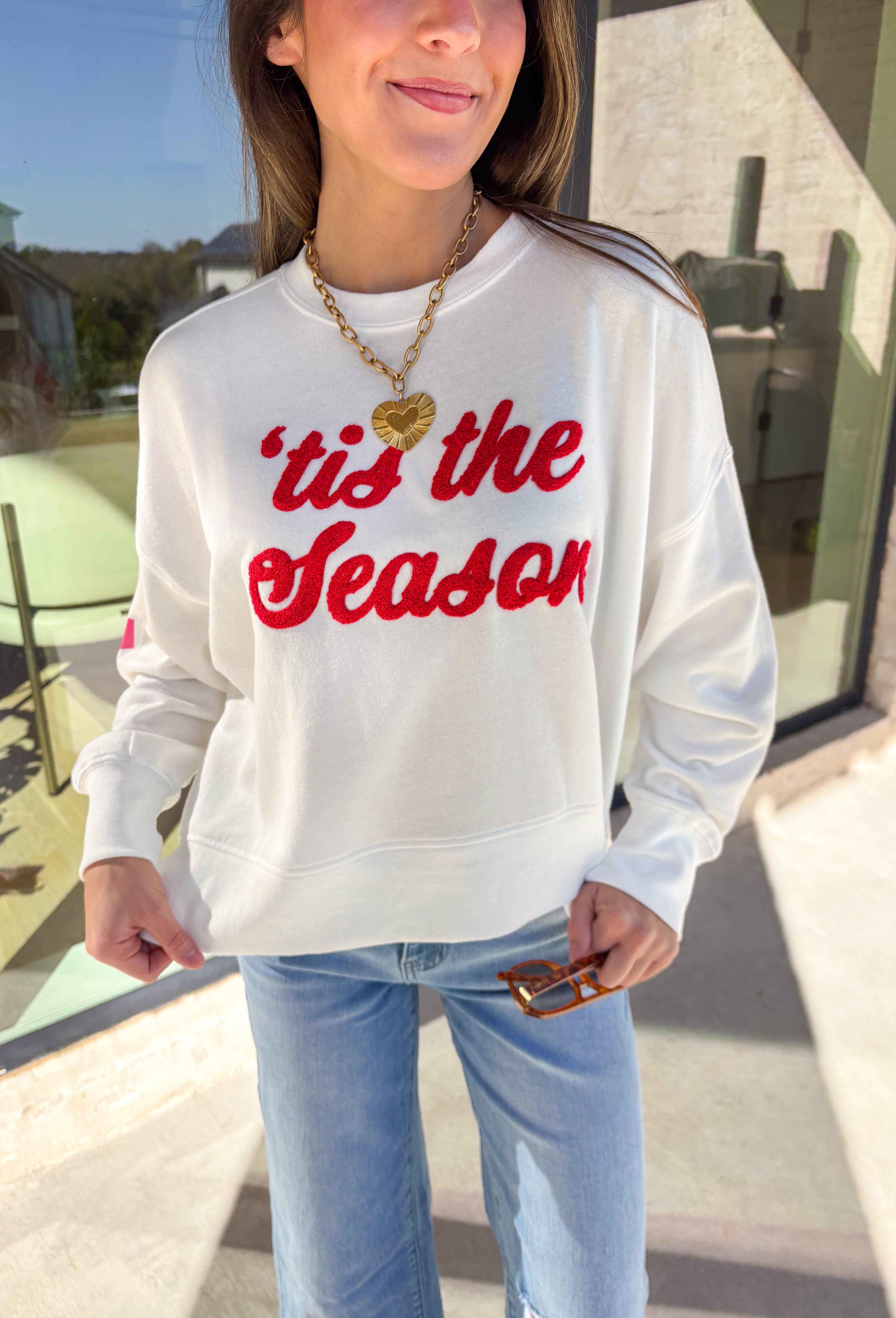 Get in the holiday spirit with this cheerful white pullover by Shiraleah! The front features a textured red “‘Tis The Season” design, while the back adds a playful surprise with a colorful “Fa La La” print. Its soft fabric and cropped fit make it the perfect piece for decking the halls or cozy nights by the fire.