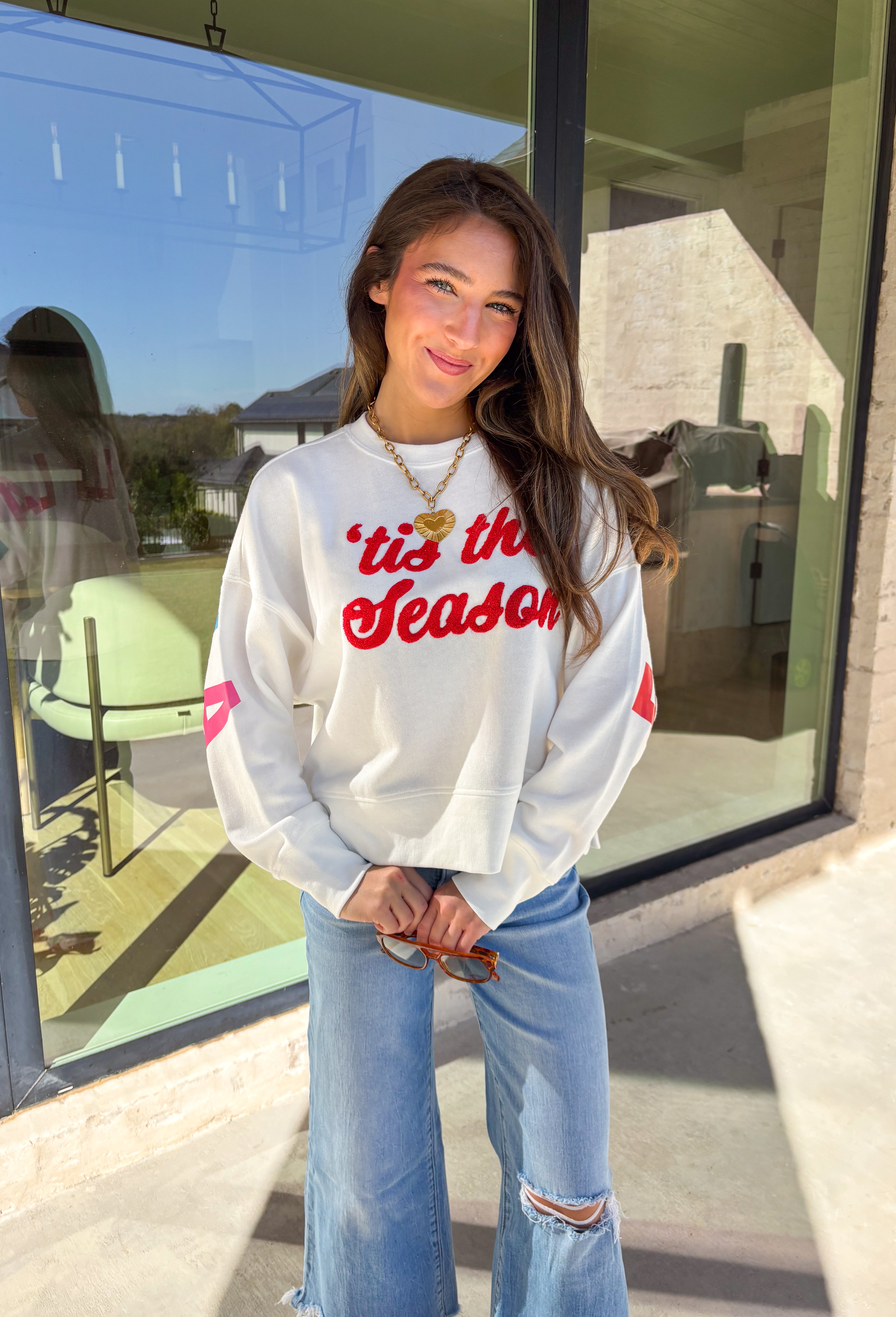 Get in the holiday spirit with this cheerful white pullover by Shiraleah! The front features a textured red “‘Tis The Season” design, while the back adds a playful surprise with a colorful “Fa La La” print. Its soft fabric and cropped fit make it the perfect piece for decking the halls or cozy nights by the fire.