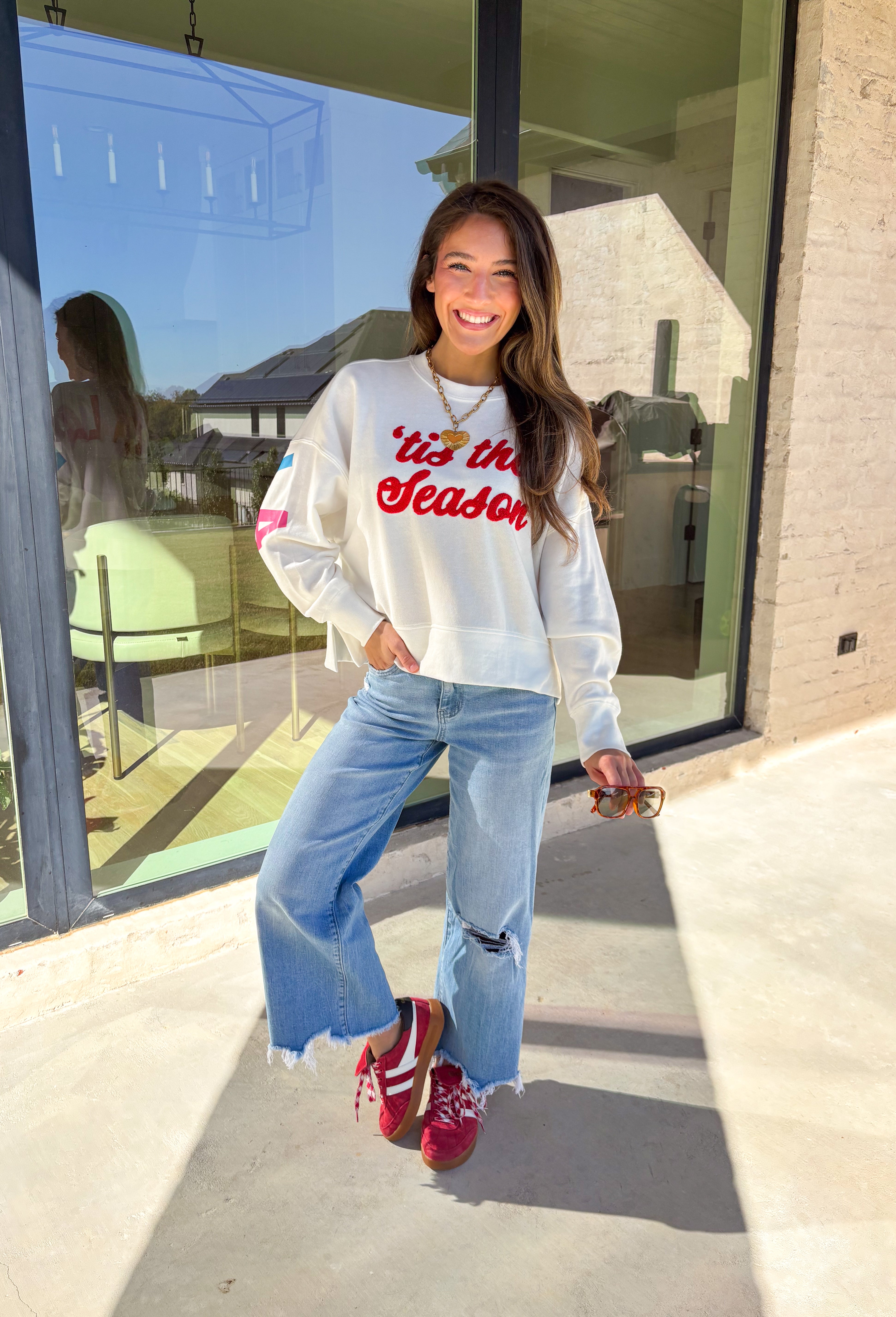 Get in the holiday spirit with this cheerful white pullover by Shiraleah! The front features a textured red “‘Tis The Season” design, while the back adds a playful surprise with a colorful “Fa La La” print. Its soft fabric and cropped fit make it the perfect piece for decking the halls or cozy nights by the fire.