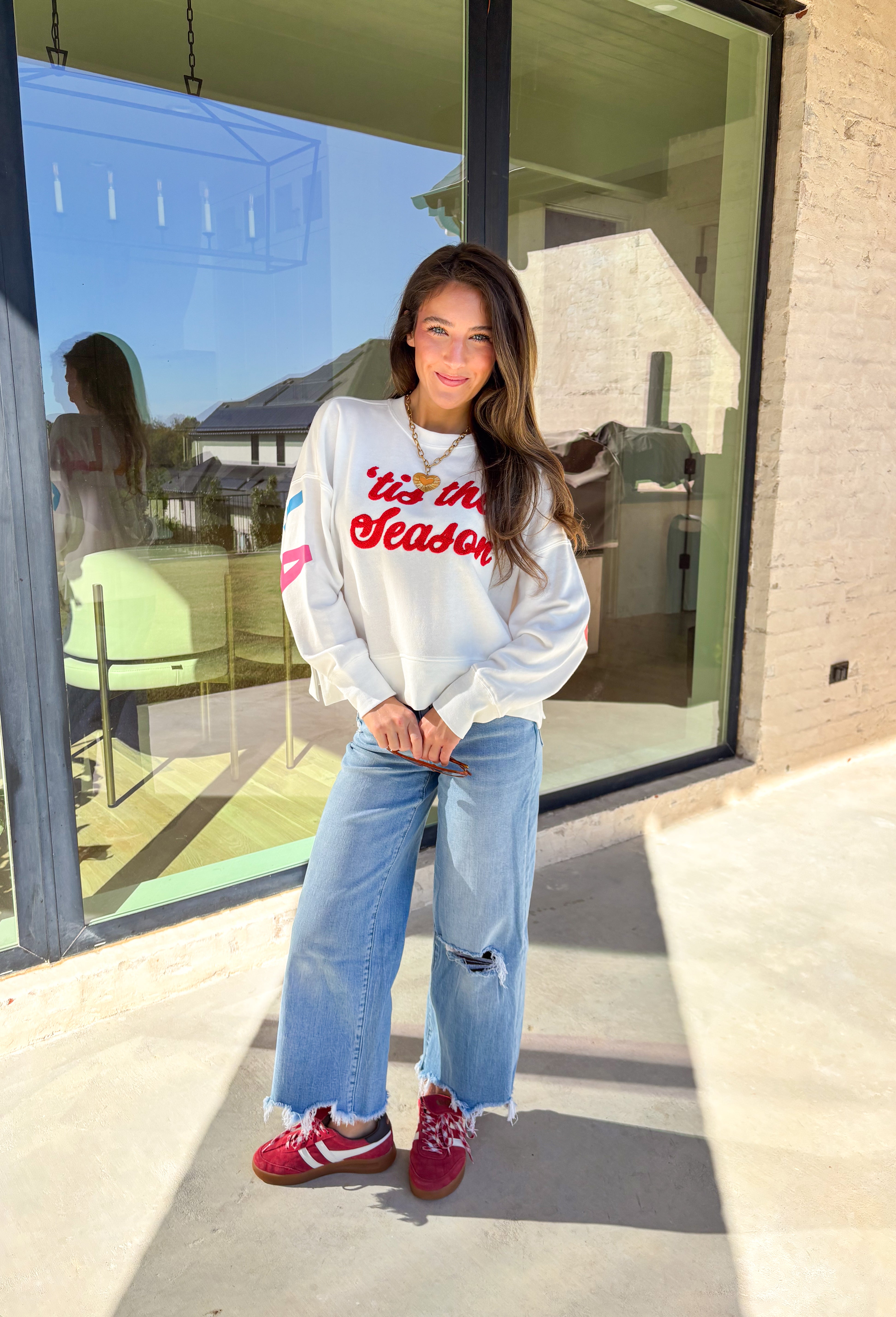 Get in the holiday spirit with this cheerful white pullover by Shiraleah! The front features a textured red “‘Tis The Season” design, while the back adds a playful surprise with a colorful “Fa La La” print. Its soft fabric and cropped fit make it the perfect piece for decking the halls or cozy nights by the fire.
