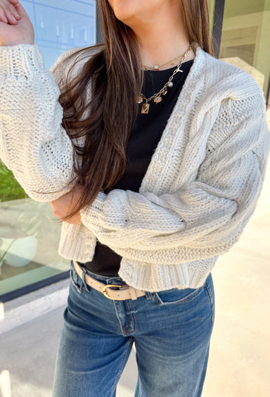 Cozy up in this off-white open-front cardigan by Double Zero. Designed with a chunky cable knit texture, this cardigan is the perfect layering piece for crisp fall days. The relaxed fit and soft feel make it a versatile staple you’ll reach for again and again—whether you’re styling it over a dress or pairing it with jeans and a tee.