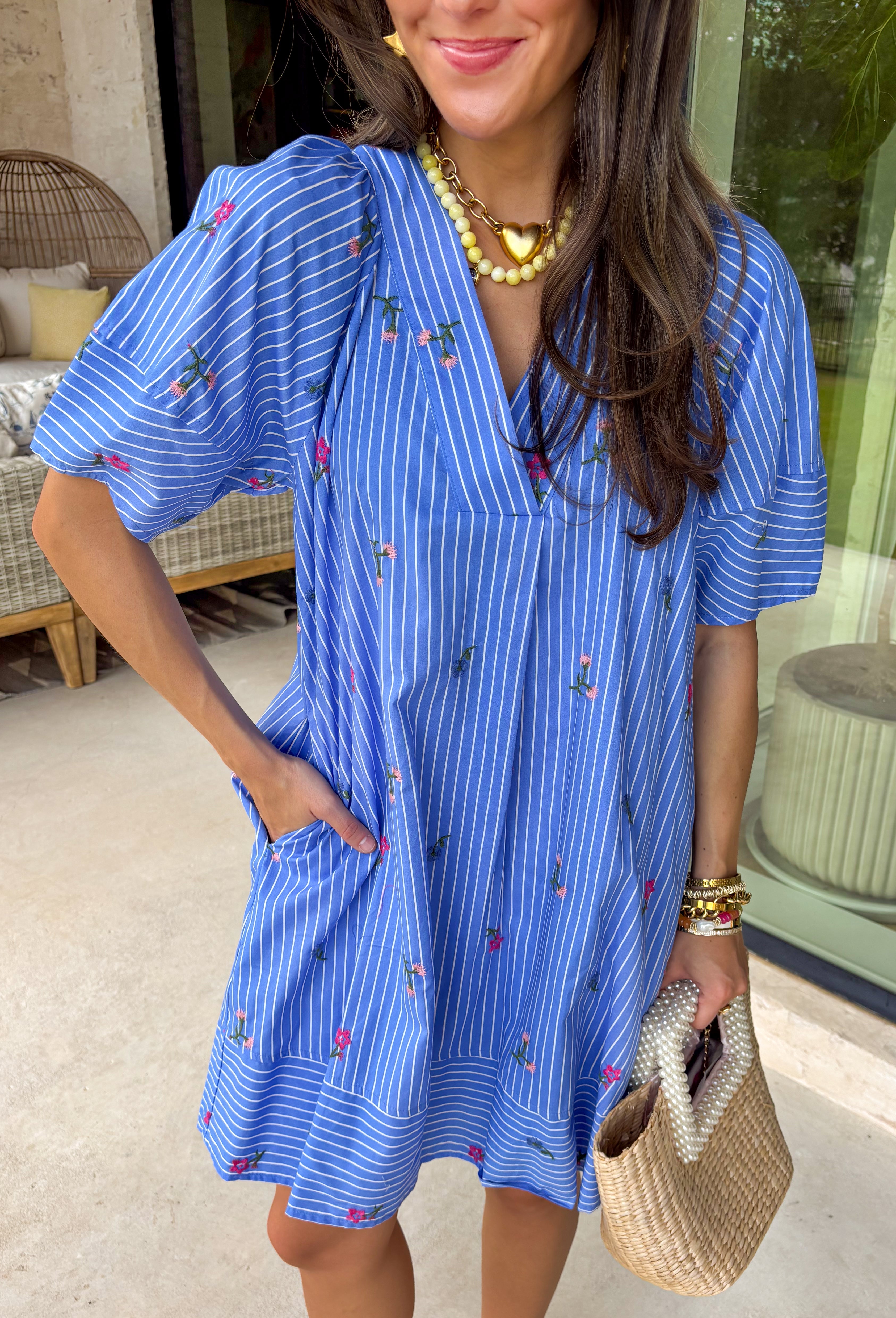 This short sleeve blue dress by Entro is the perfect mix of classic stripes and sweet spring details. Featuring a crisp white stripe print throughout, it’s bright, timeless, and easy to wear—but the embroidered floral design takes it to the next level. With pops of pink, blue, and green stitched throughout, it has that extra-special feel while still being totally everyday-friendly. The fit is comfortable and effortless, plus it’s fully lined for easy wear and confidence.