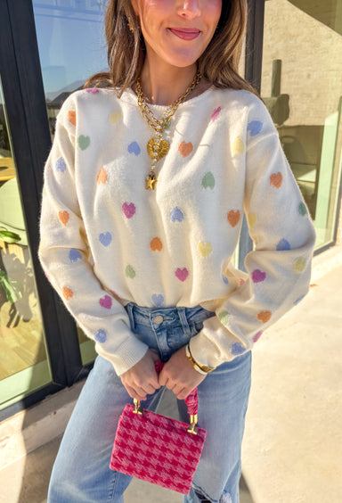Sweet, cheerful, and full of love, this cream sweater by Sunday Edition is perfect for Valentine’s Day and beyond. Featuring a colorful heart print in shades of orange, pink, yellow, green, and blue, this cozy knit brings a fun pop of color to your wardrobe. Soft and lightweight with an easy fit, it’s the kind of sweater that feels festive for February but still cute all season long.
