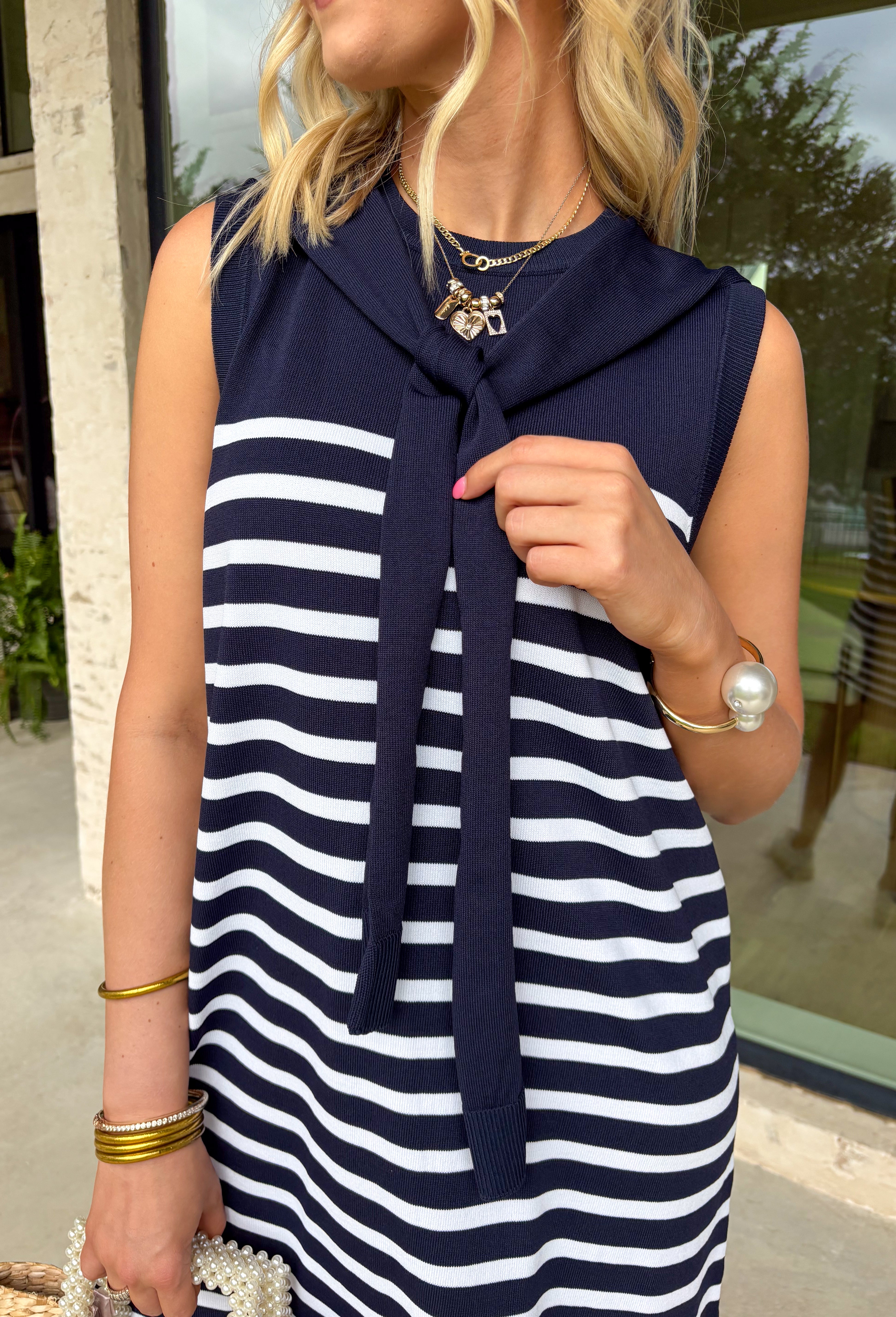 Polished with a playful twist! This navy sleeveless dress features a timeless white stripe print and a unique knit scarf tie detail at the neckline that instantly elevates the look. It’s classic, but with just enough personality to stand out. The sleeveless silhouette keeps it sleek and versatile, while the soft knit fabric offers a comfortable, flattering drape. Whether you’re heading to brunch, the office, or a weekend getaway, this dress makes getting dressed feel effortless and put-together.