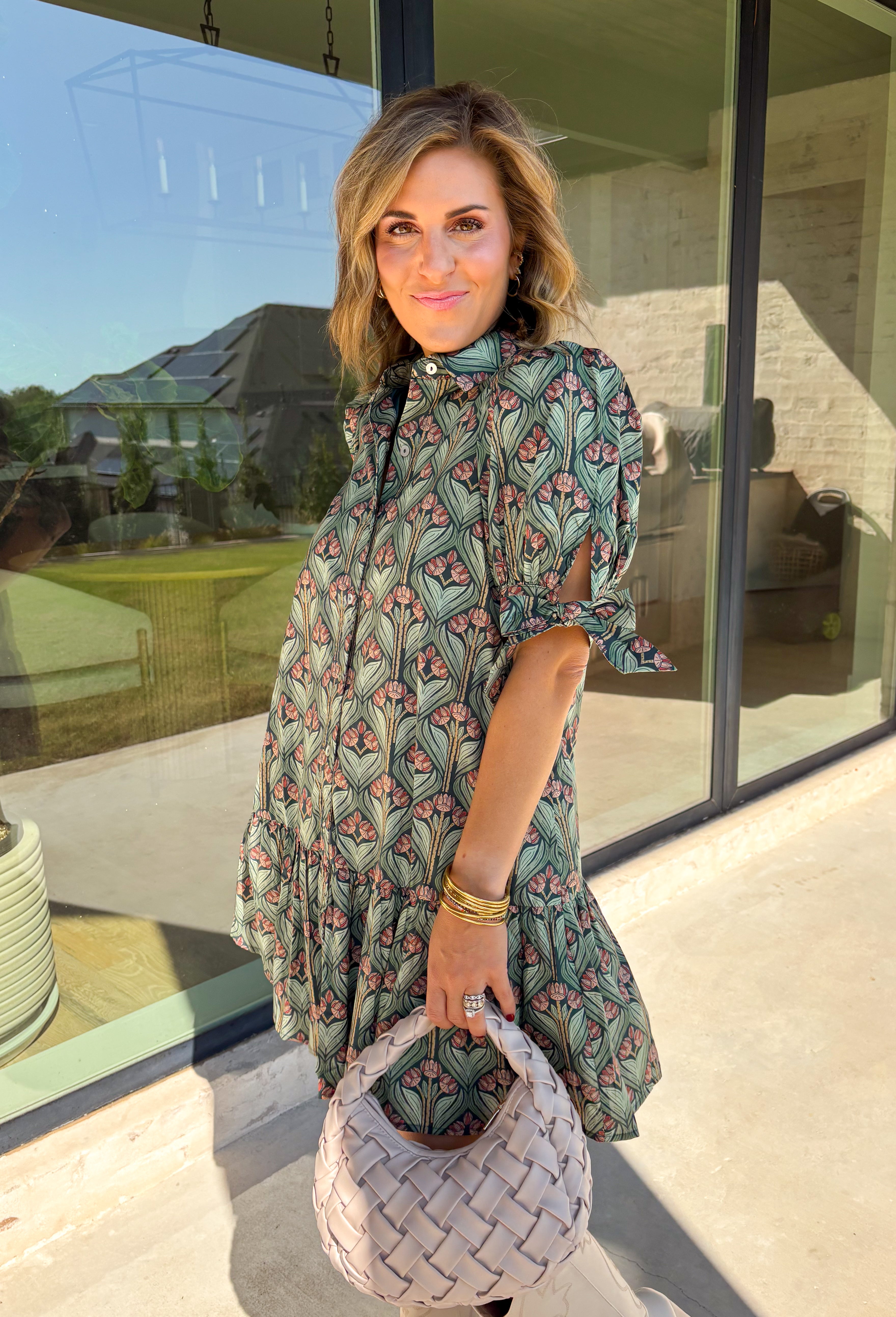 Embrace the beauty of the season in this charming dress from Entro. Featuring a gorgeous floral print in shades of hunter green, muted green, peach, and brown, this feminine dress is perfect for everything from weekend brunches to seasonal celebrations. The button-front design and flattering neckline create a timeless silhouette, while the ¾ puff sleeves with delicate tie details add a playful touch. 
