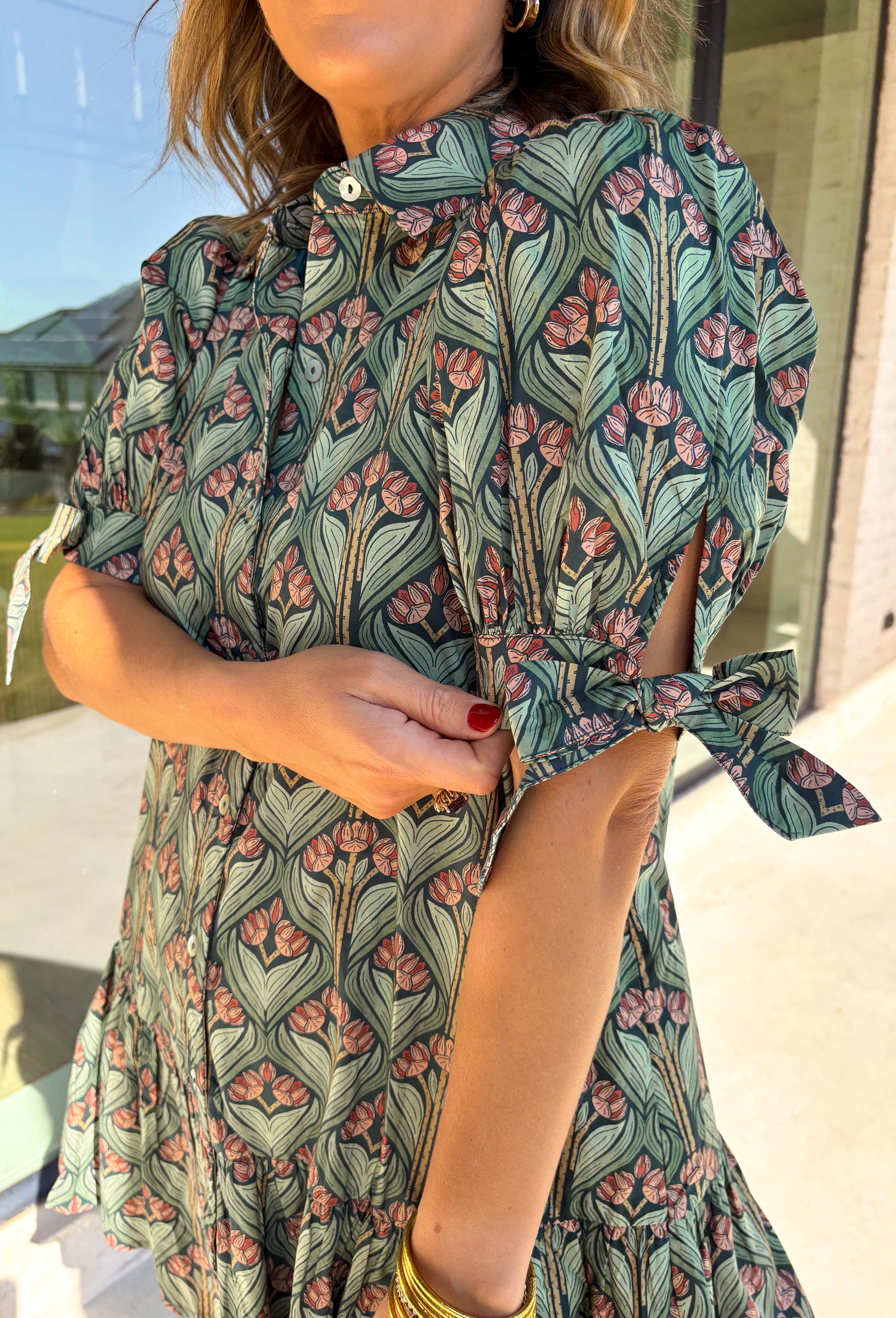Embrace the beauty of the season in this charming dress from Entro. Featuring a gorgeous floral print in shades of hunter green, muted green, peach, and brown, this feminine dress is perfect for everything from weekend brunches to seasonal celebrations. The button-front design and flattering neckline create a timeless silhouette, while the ¾ puff sleeves with delicate tie details add a playful touch. 