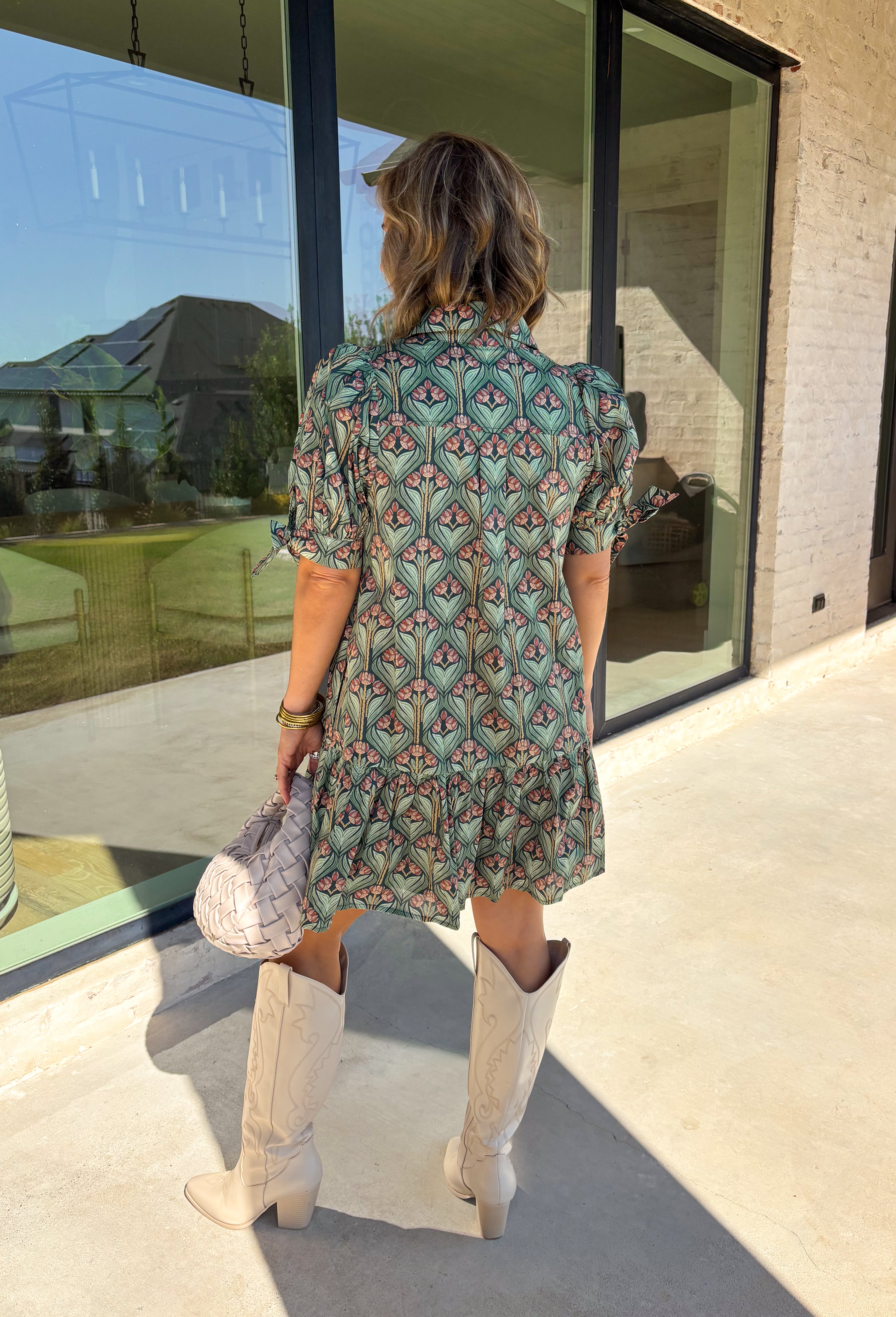 Embrace the beauty of the season in this charming dress from Entro. Featuring a gorgeous floral print in shades of hunter green, muted green, peach, and brown, this feminine dress is perfect for everything from weekend brunches to seasonal celebrations. The button-front design and flattering neckline create a timeless silhouette, while the ¾ puff sleeves with delicate tie details add a playful touch. 