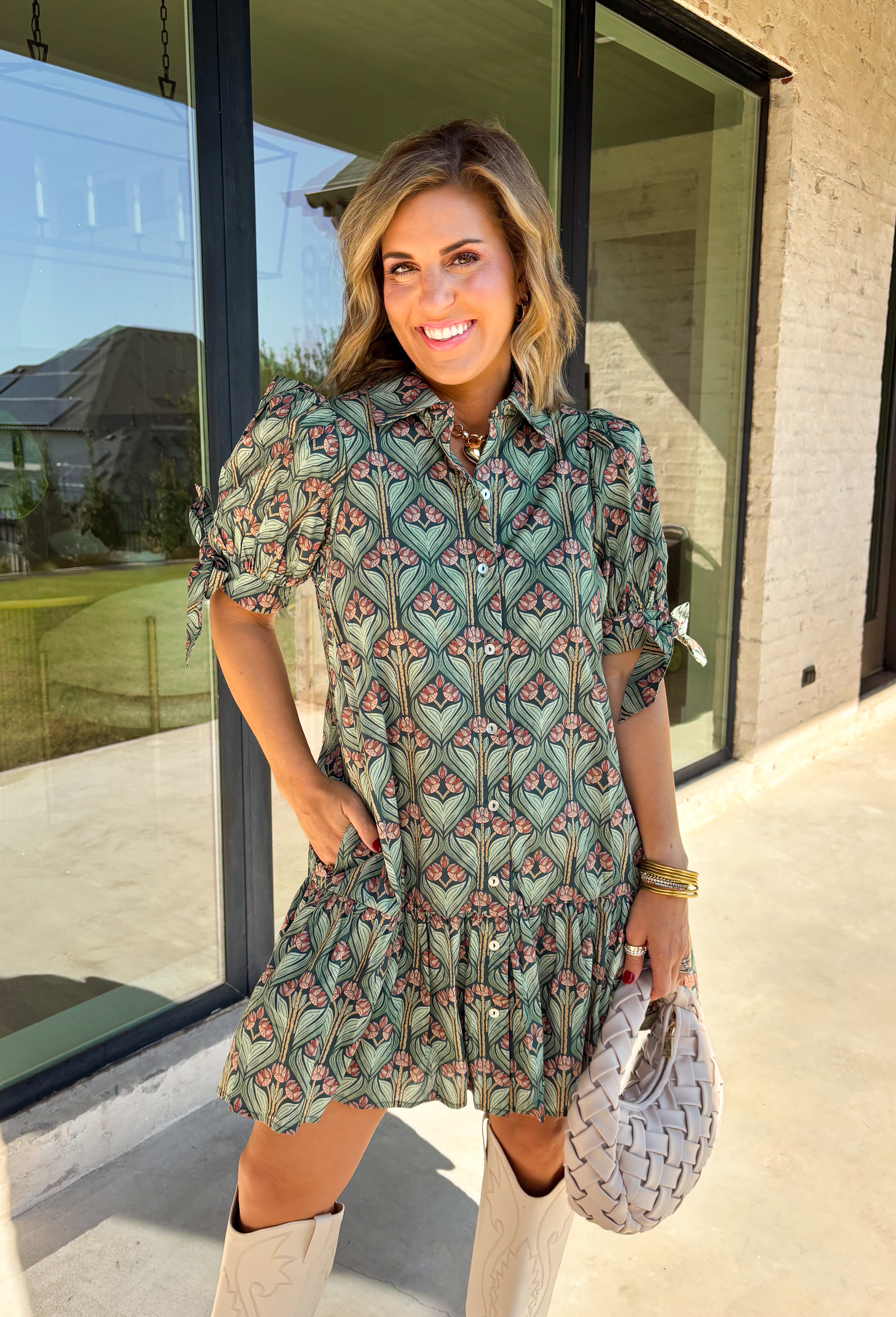 Embrace the beauty of the season in this charming dress from Entro. Featuring a gorgeous floral print in shades of hunter green, muted green, peach, and brown, this feminine dress is perfect for everything from weekend brunches to seasonal celebrations. The button-front design and flattering neckline create a timeless silhouette, while the ¾ puff sleeves with delicate tie details add a playful touch. 