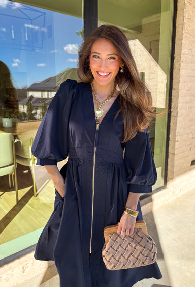 Breeze into spring with this effortlessly chic navy midi dress by Entro. Designed with 3/4 length puff sleeves and soft pleating throughout, this dress offers a timeless yet playful silhouette that’s perfect for sunny afternoons or special occasions. The front zipper closure adds a modern twist, while the lightweight fabric keeps things easy and comfortable for all-day wear.