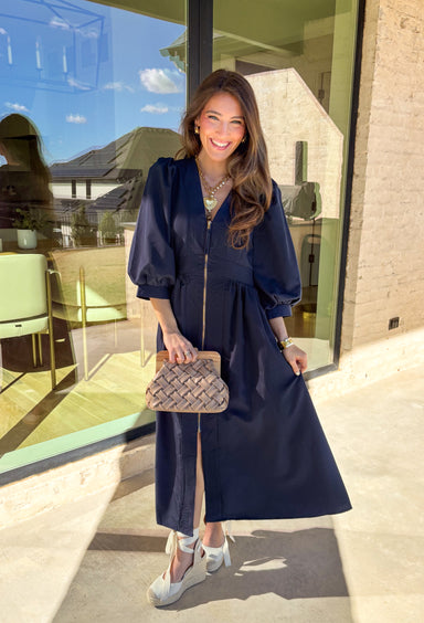 Breeze into spring with this effortlessly chic navy midi dress by Entro. Designed with 3/4 length puff sleeves and soft pleating throughout, this dress offers a timeless yet playful silhouette that’s perfect for sunny afternoons or special occasions. The front zipper closure adds a modern twist, while the lightweight fabric keeps things easy and comfortable for all-day wear.