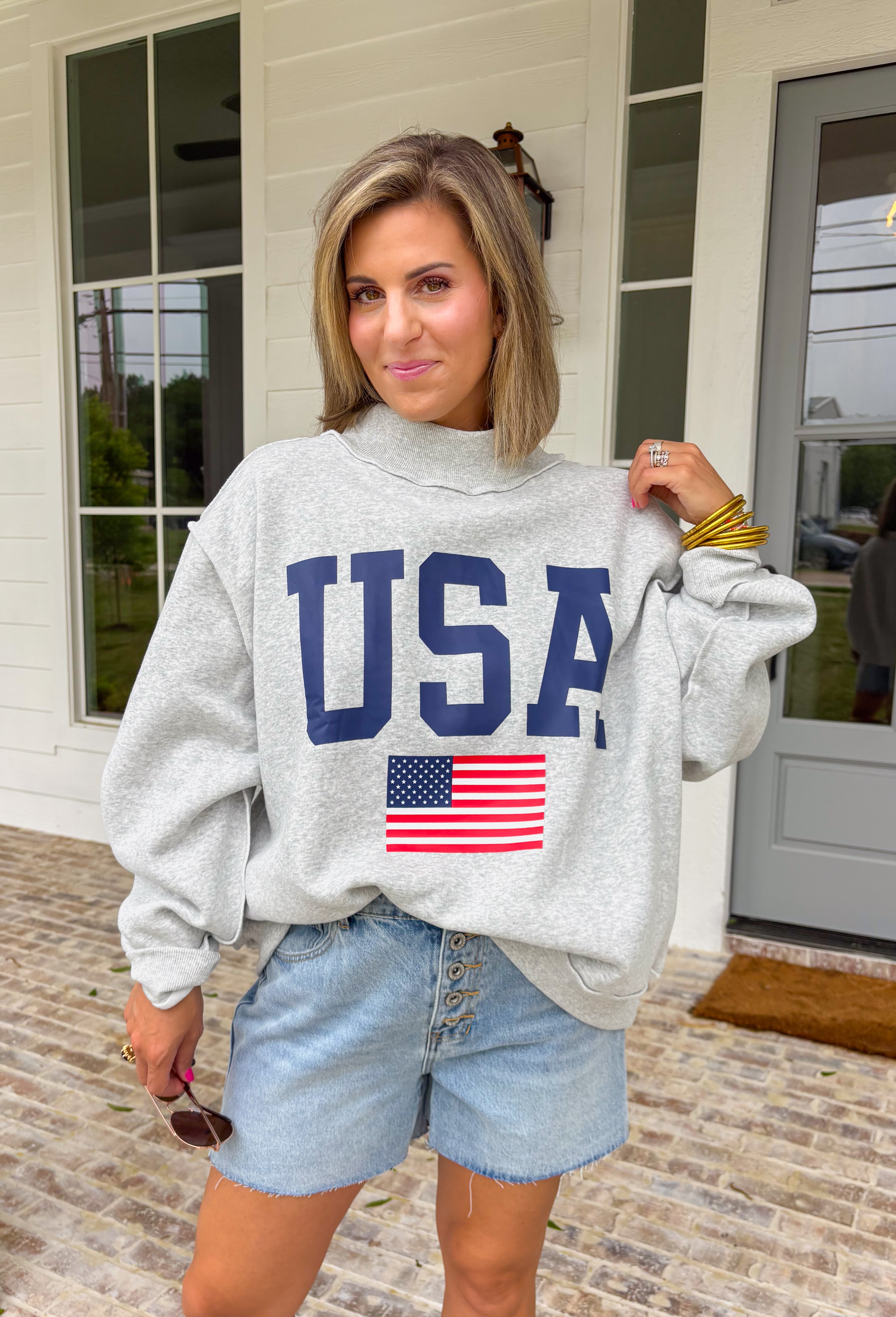 This grey reversible pullover is the ultimate cozy-meets-festive piece for your summer celebrations! Designed with two looks in one, one side features “USA” in navy with a flag design, while the other side is fleece lined with “America” in blue for a softer, cozier feel. The mock neck adds an elevated touch, making it perfect for those cooler summer nights—think fireworks, lake evenings, or early morning coffee runs. It’s an easy throw-on layer that still feels fun and patriotic. 