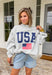 This grey reversible pullover is the ultimate cozy-meets-festive piece for your summer celebrations! Designed with two looks in one, one side features “USA” in navy with a flag design, while the other side is fleece lined with “America” in blue for a softer, cozier feel. The mock neck adds an elevated touch, making it perfect for those cooler summer nights—think fireworks, lake evenings, or early morning coffee runs. It’s an easy throw-on layer that still feels fun and patriotic. 