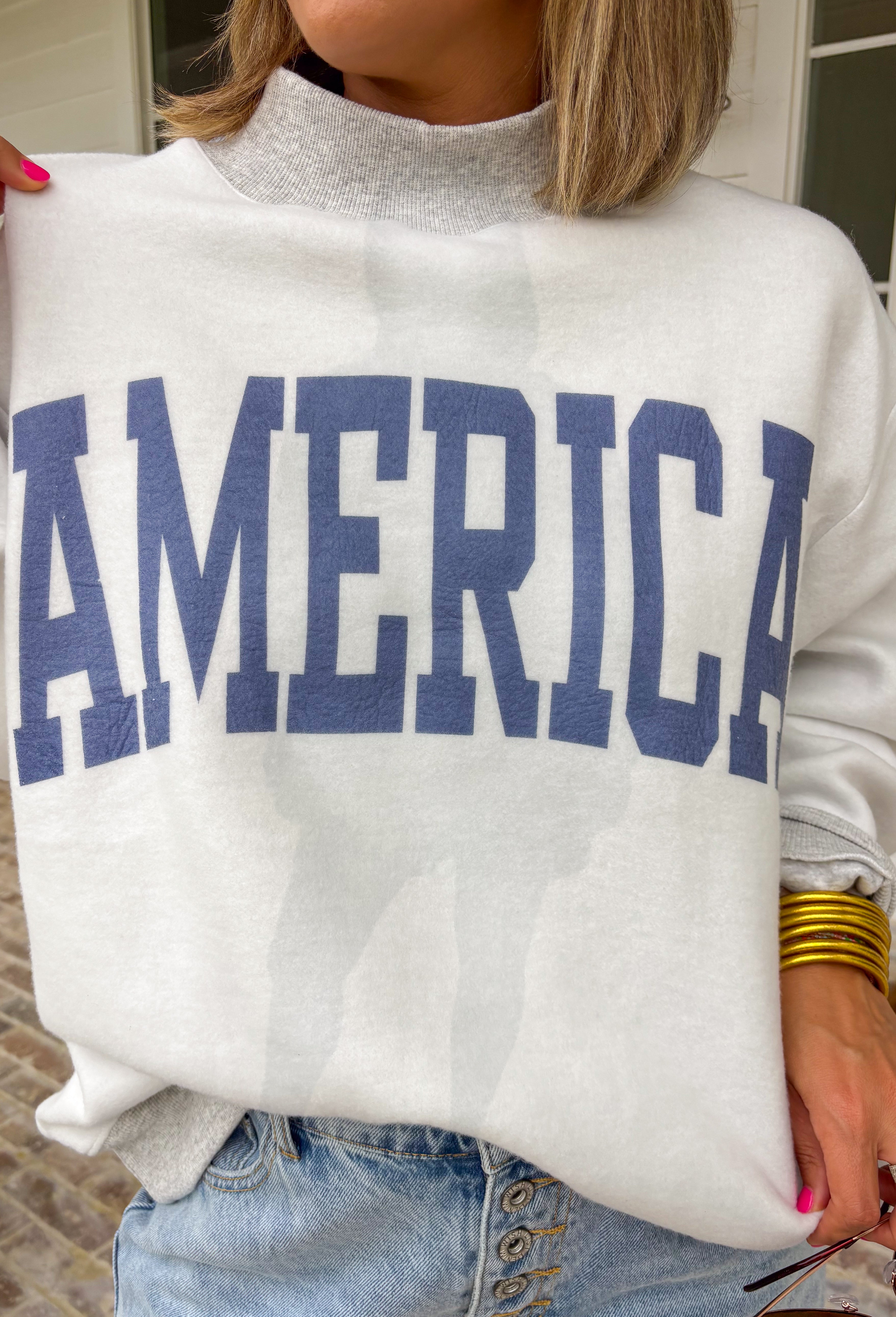 This grey reversible pullover is the ultimate cozy-meets-festive piece for your summer celebrations! Designed with two looks in one, one side features “USA” in navy with a flag design, while the other side is fleece lined with “America” in blue for a softer, cozier feel. The mock neck adds an elevated touch, making it perfect for those cooler summer nights—think fireworks, lake evenings, or early morning coffee runs. It’s an easy throw-on layer that still feels fun and patriotic. 