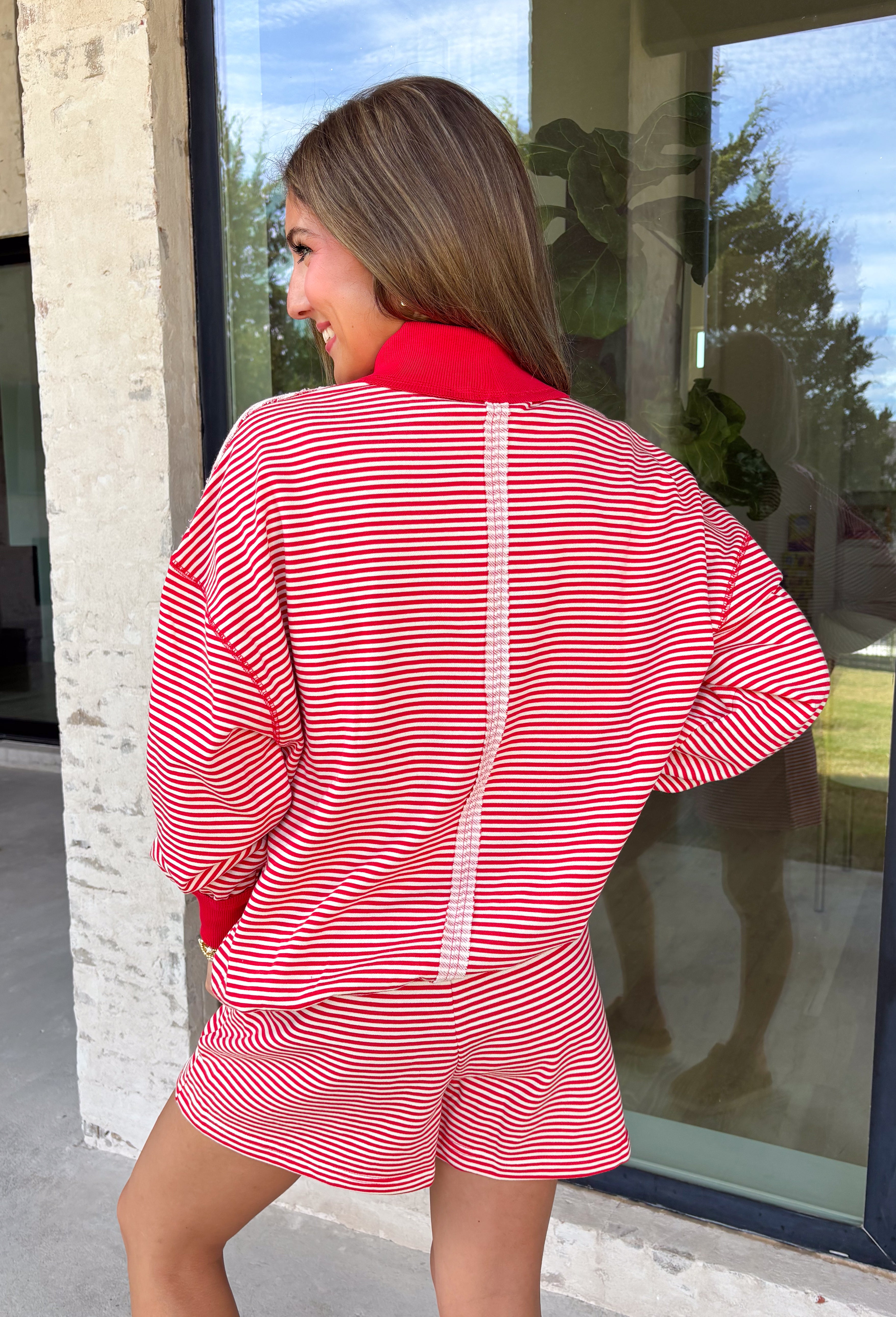 Cozy holiday mornings just found their new uniform with this red and white striped two-piece set from Tres Bien. The oversized long sleeve pullover features a mock neckline with red ribbed trim along the neckline, cuffs, and hem for a festive pop of color. Matching shorts keep the look relaxed and comfortable with an elastic waistband and adjustable drawstring detail. 