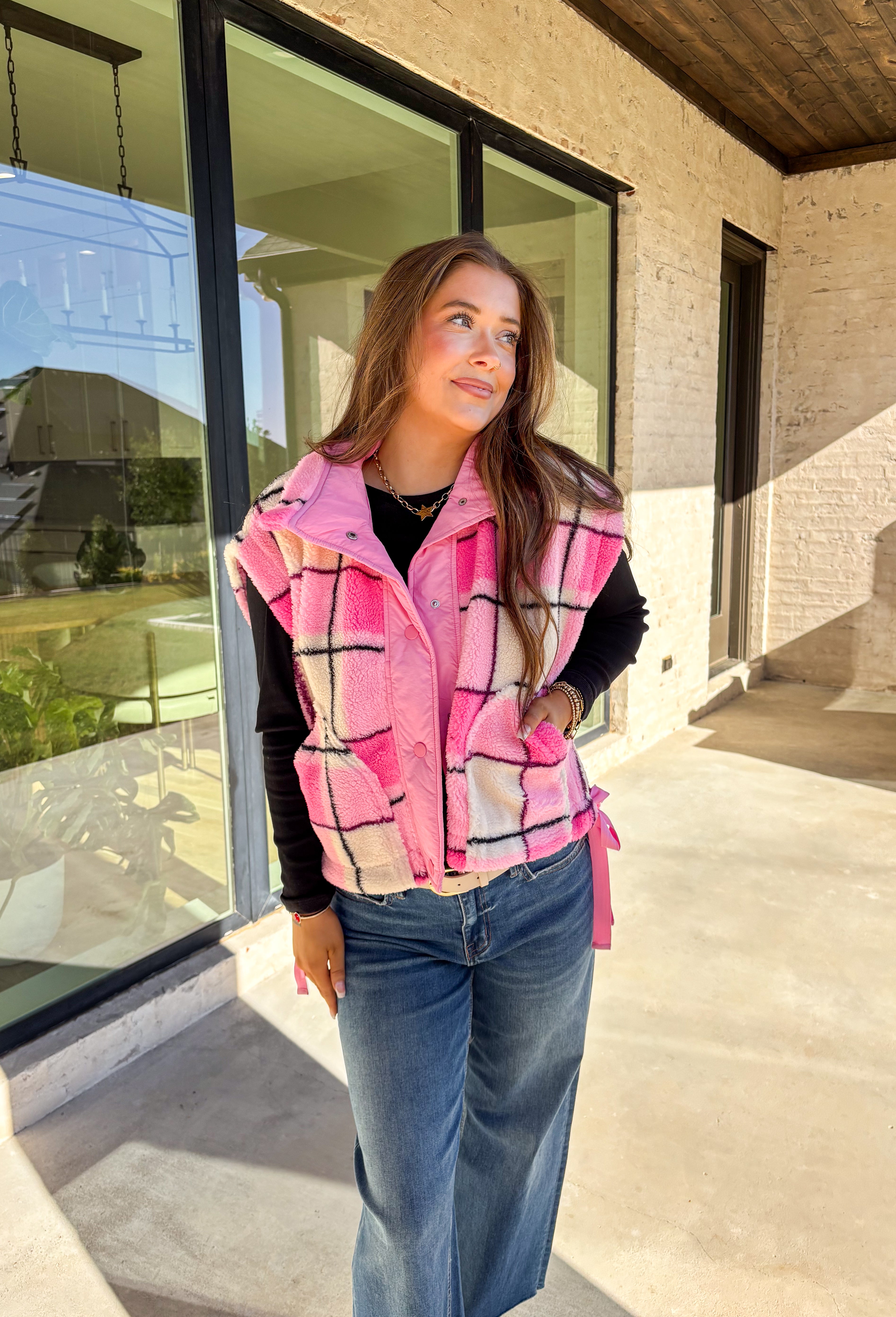 Get bundled up in cuteness with this cozy pink and white plaid vest! With sweet pops of black in the pattern and darling pink bow ties on each side, it brings just the right amount of charm to your cold-weather wardrobe. Whether you're layering it over a long sleeve tee or a chunky knit sweater, this vest is ready to warm things up in the coziest way.