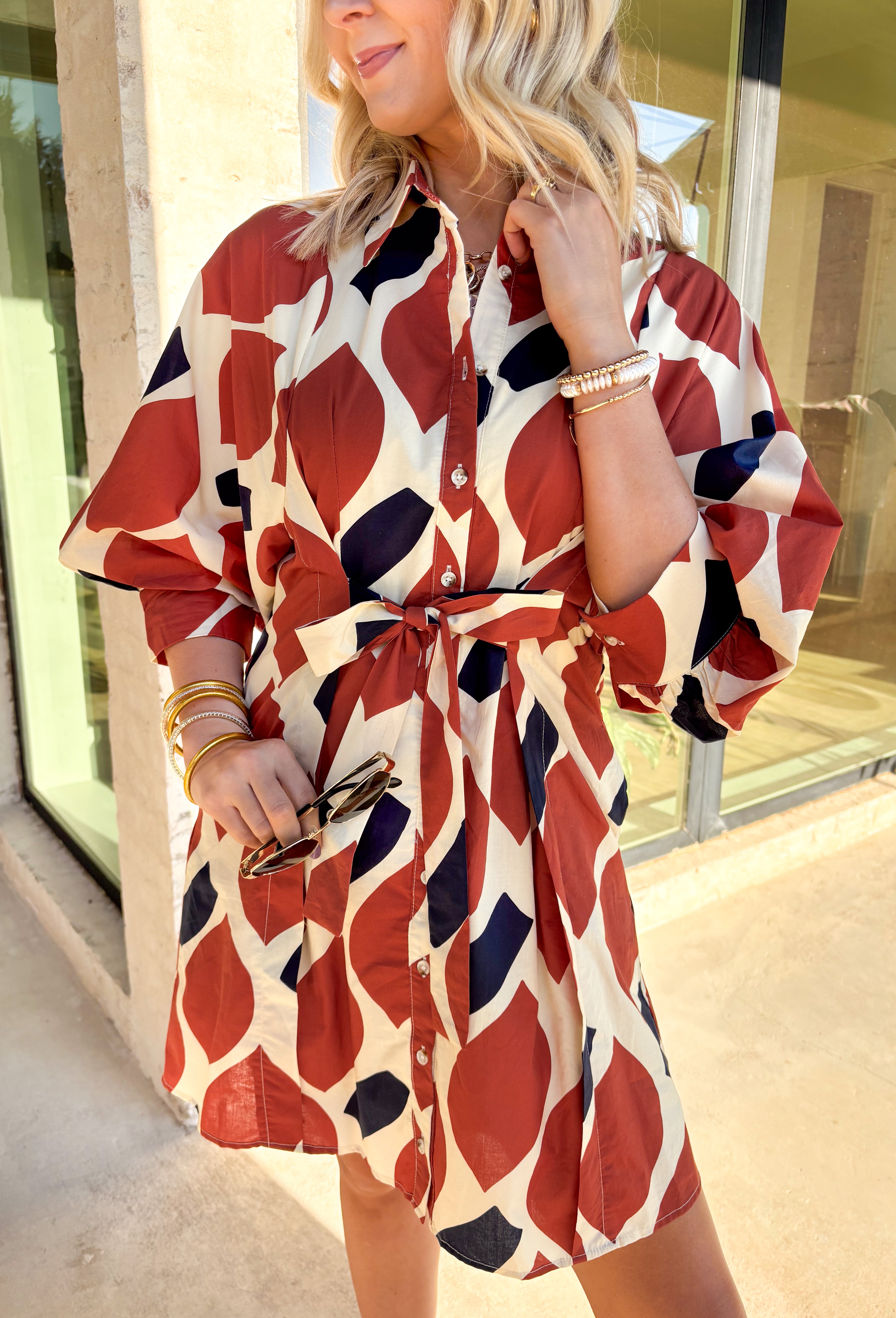 This printed mini dress by Entro is the perfect mix of classic and playful. Designed in warm tones of ecru, rust, and navy, it features a flattering self-tie waist and a structured shirt collar for a polished look. The ¾ sleeves and button-front closure add timeless charm, while side pockets and a full lining make it comfortable for everyday wear. A versatile piece that transitions effortlessly from workdays to weekend plans.