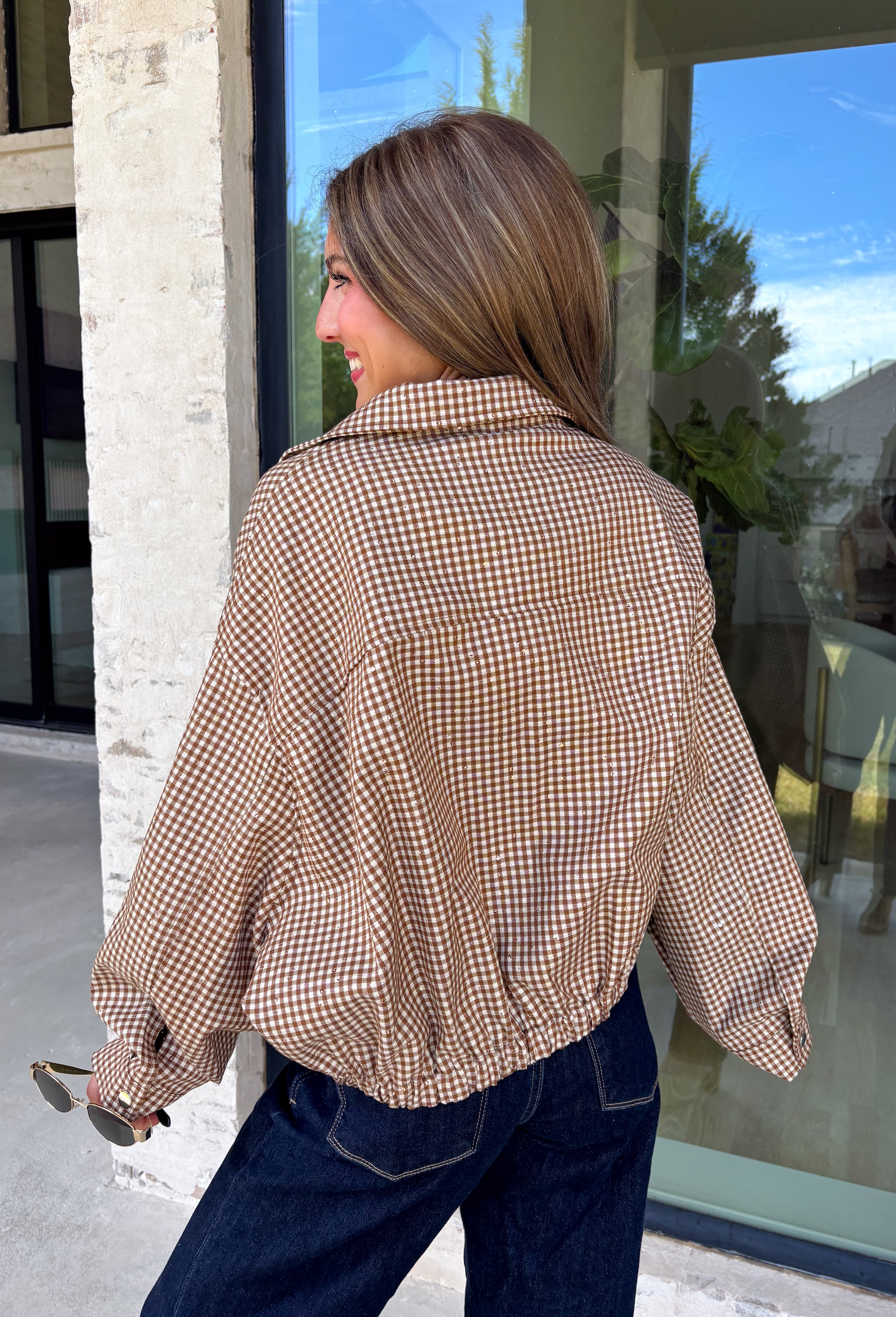Classic gingham gets a fun fall refresh with this camel and cream jacket from Glam. The neutral checkered print keeps it easy to style, while sequin stitching throughout adds just the right amount of sparkle when it catches the light. A collared neckline and both zipper and button closures give it a structured, jacket-inspired look, while the elastic back hem creates a comfortable shape.