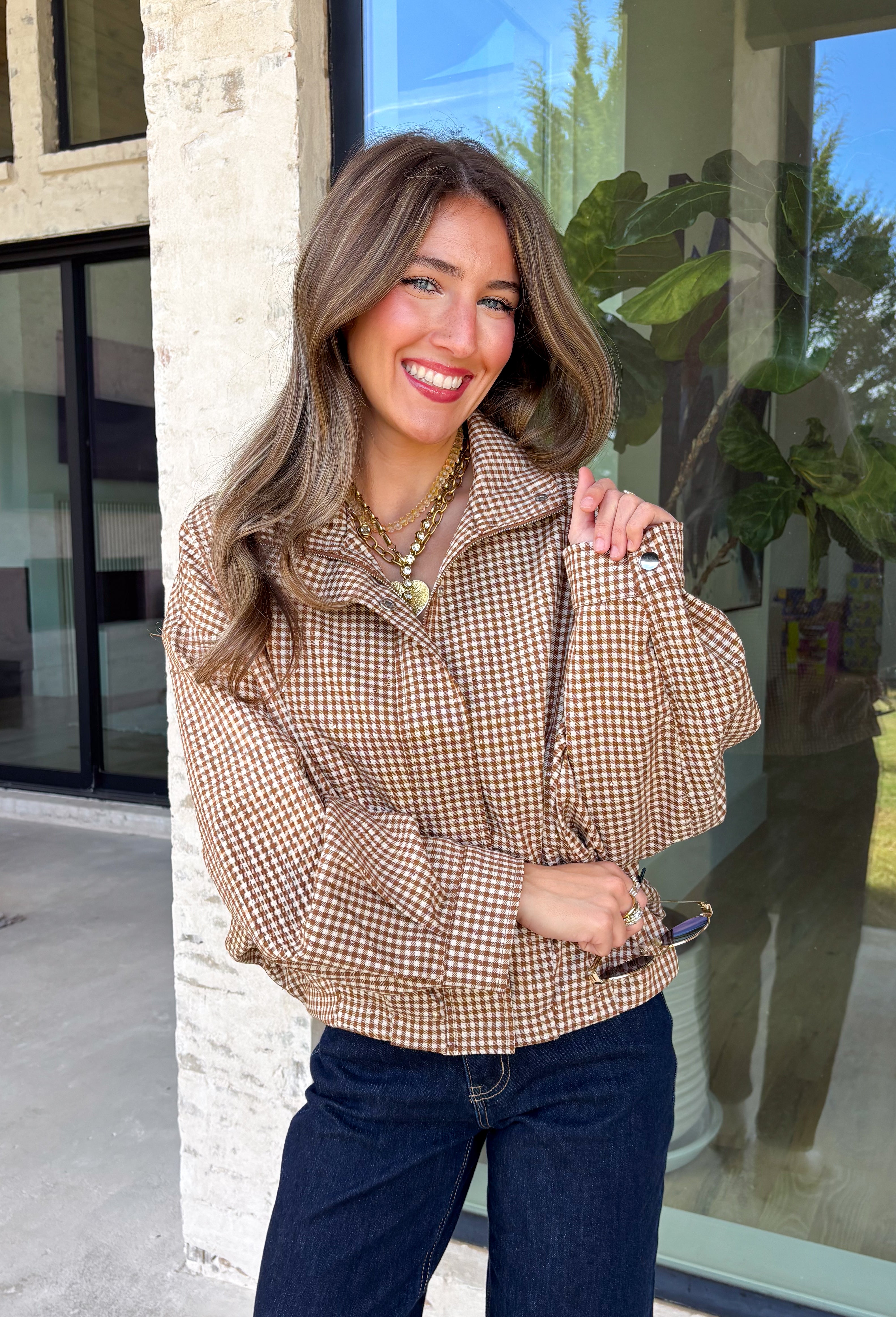 Classic gingham gets a fun fall refresh with this camel and cream jacket from Glam. The neutral checkered print keeps it easy to style, while sequin stitching throughout adds just the right amount of sparkle when it catches the light. A collared neckline and both zipper and button closures give it a structured, jacket-inspired look, while the elastic back hem creates a comfortable shape.